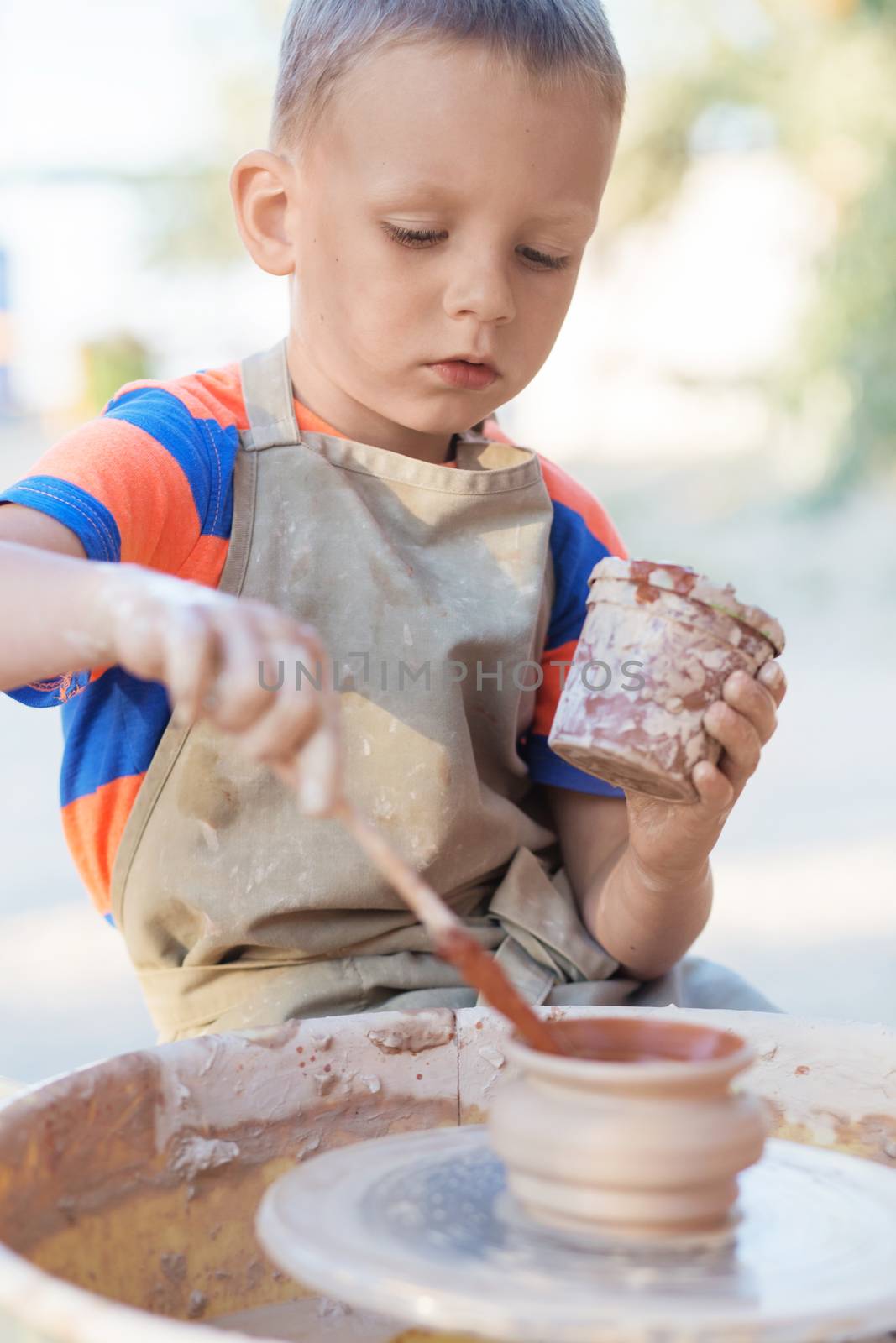 Hands of young potter, creating an earthen jar on the circle, close-up. Little smiling boy produced on potters wheel pot
