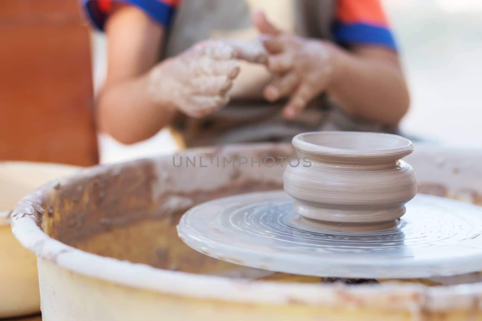 Hands of young potter, creating an earthen jar on the circle, close-up