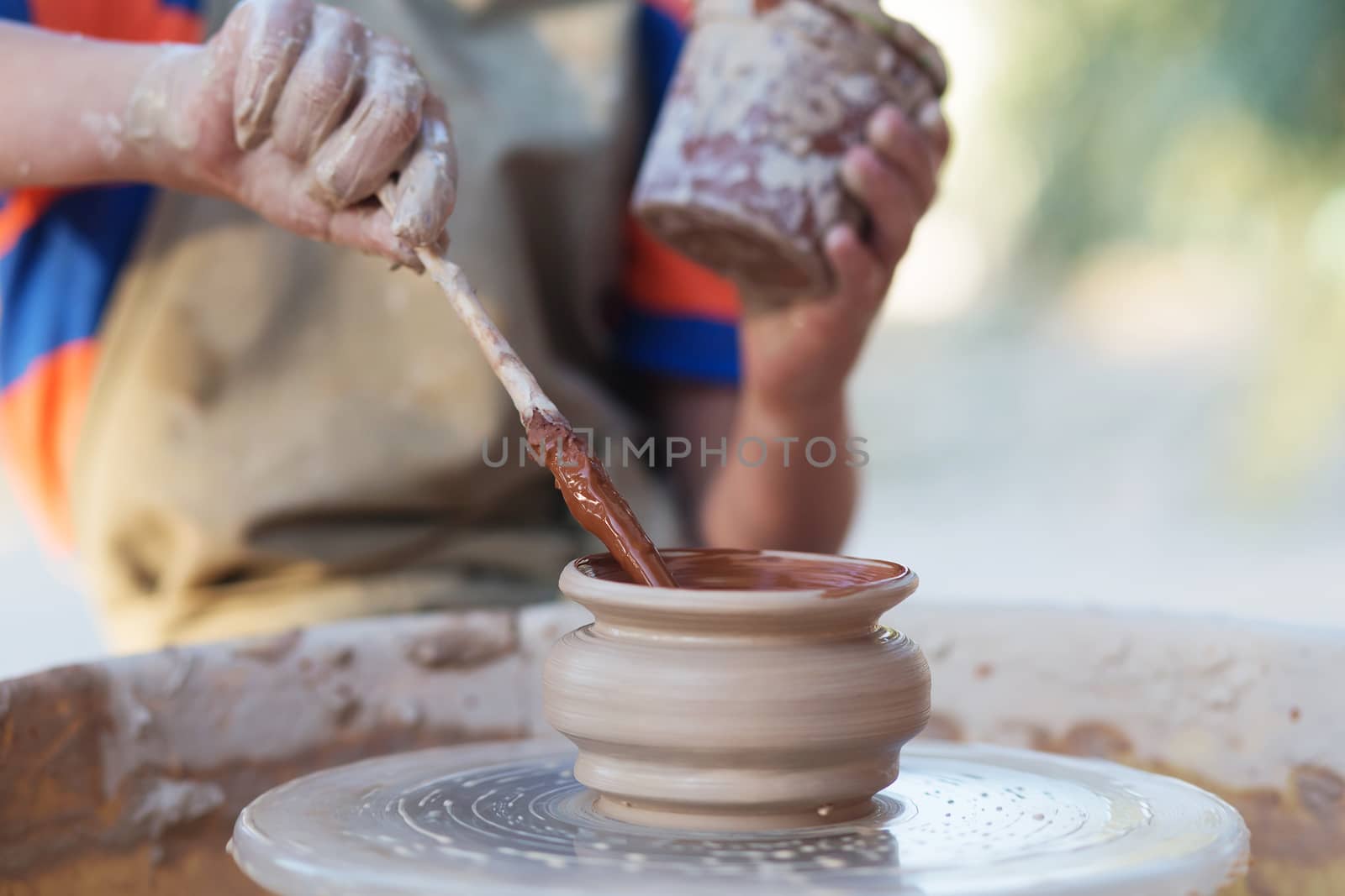 Hands of young potter, creating an earthen jar on the circle, close-up