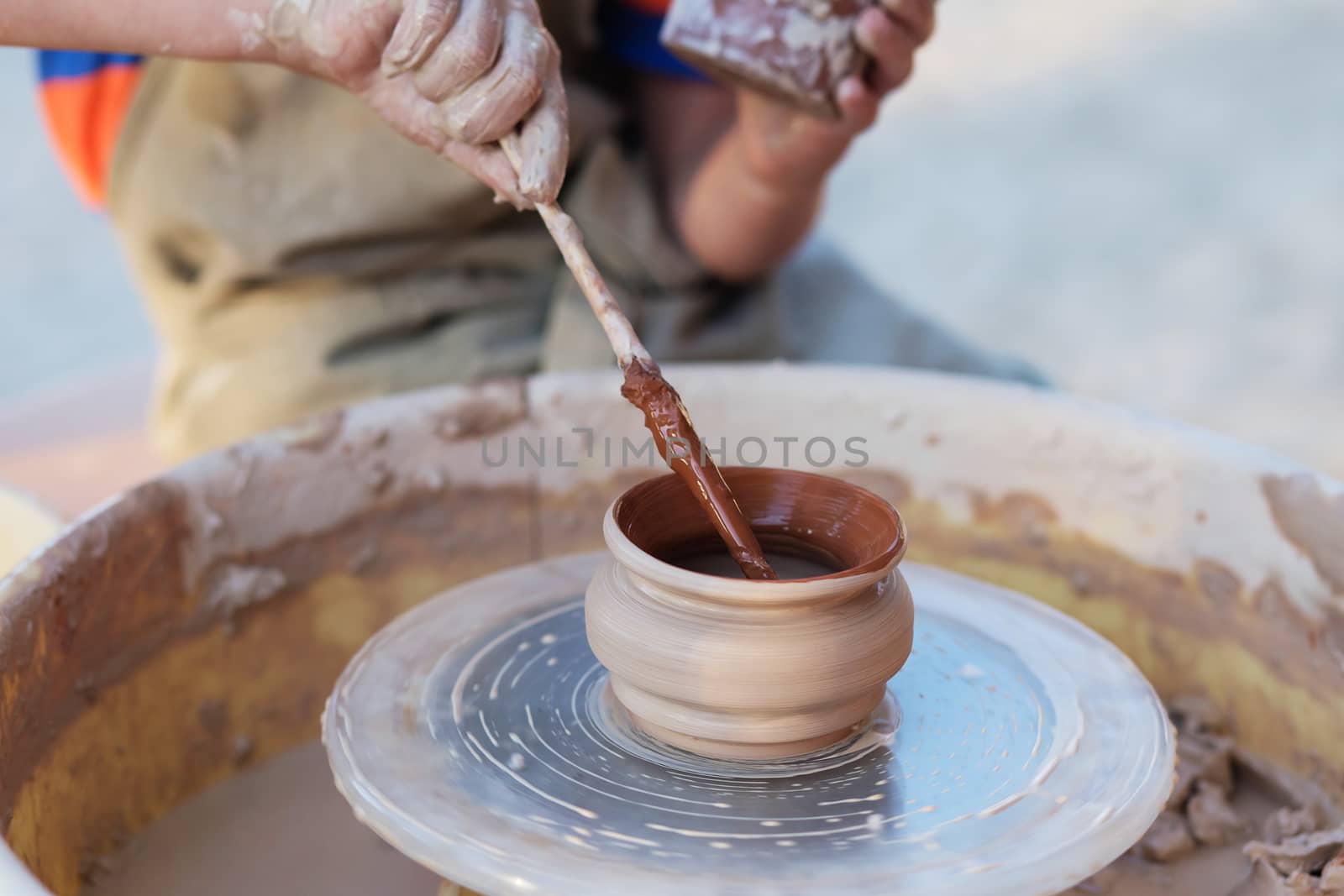 Hands of young potter, creating an earthen jar on the circle, close-up