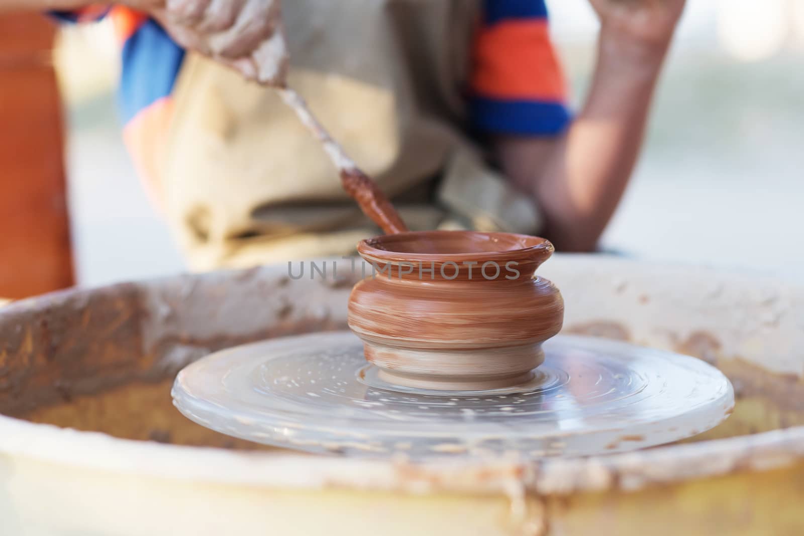 Hands of young potter, creating an earthen jar on the circle, close-up