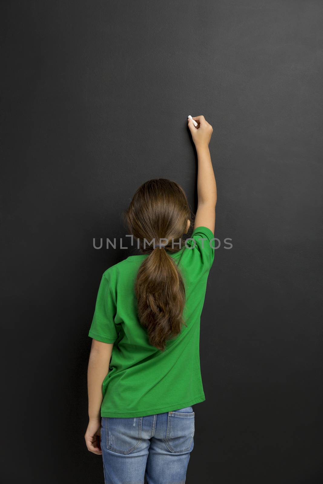 Cute little girl writing in a blackboard, with copy space.