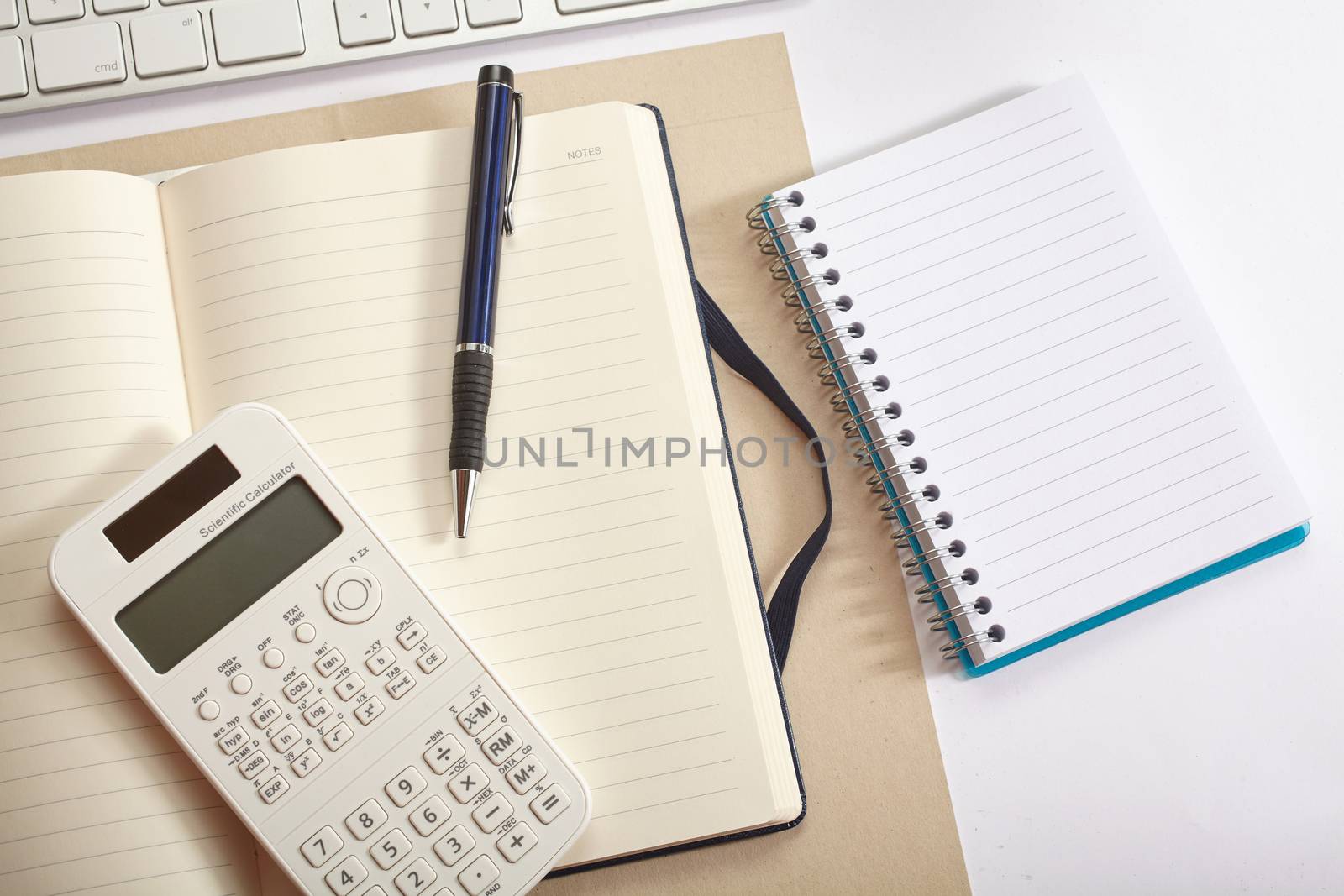 Top view office workplace - keyboard, calculator, pen, flower and notebook on white table