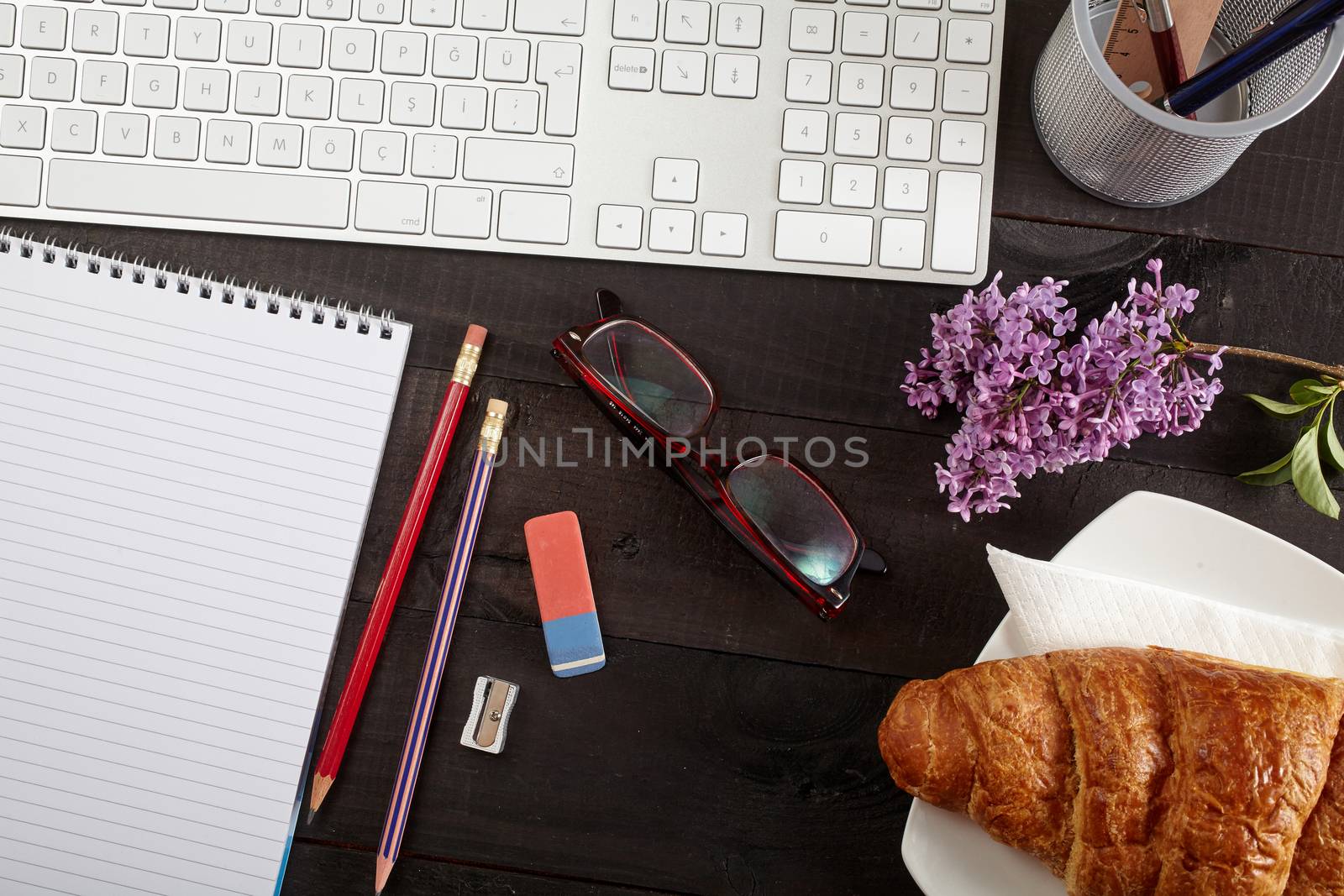 Top view office workplace - keyboard, pencil, glasses, croissant and notebook on black table