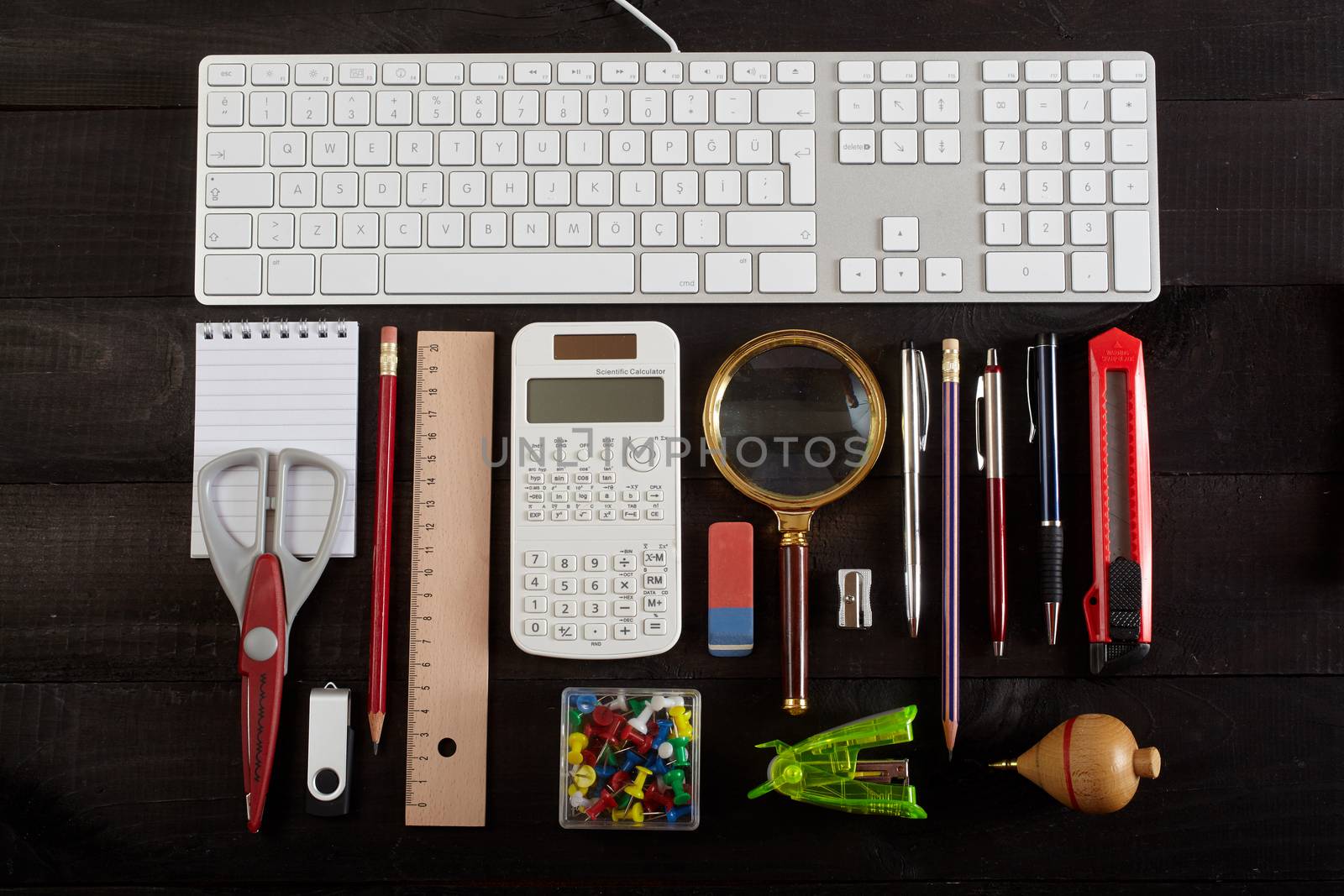 Top view office workplace - keyboard, pencil, calculator, ruler, magnifying glass, pen, cutter, scissors, whirligig and notebook on black table