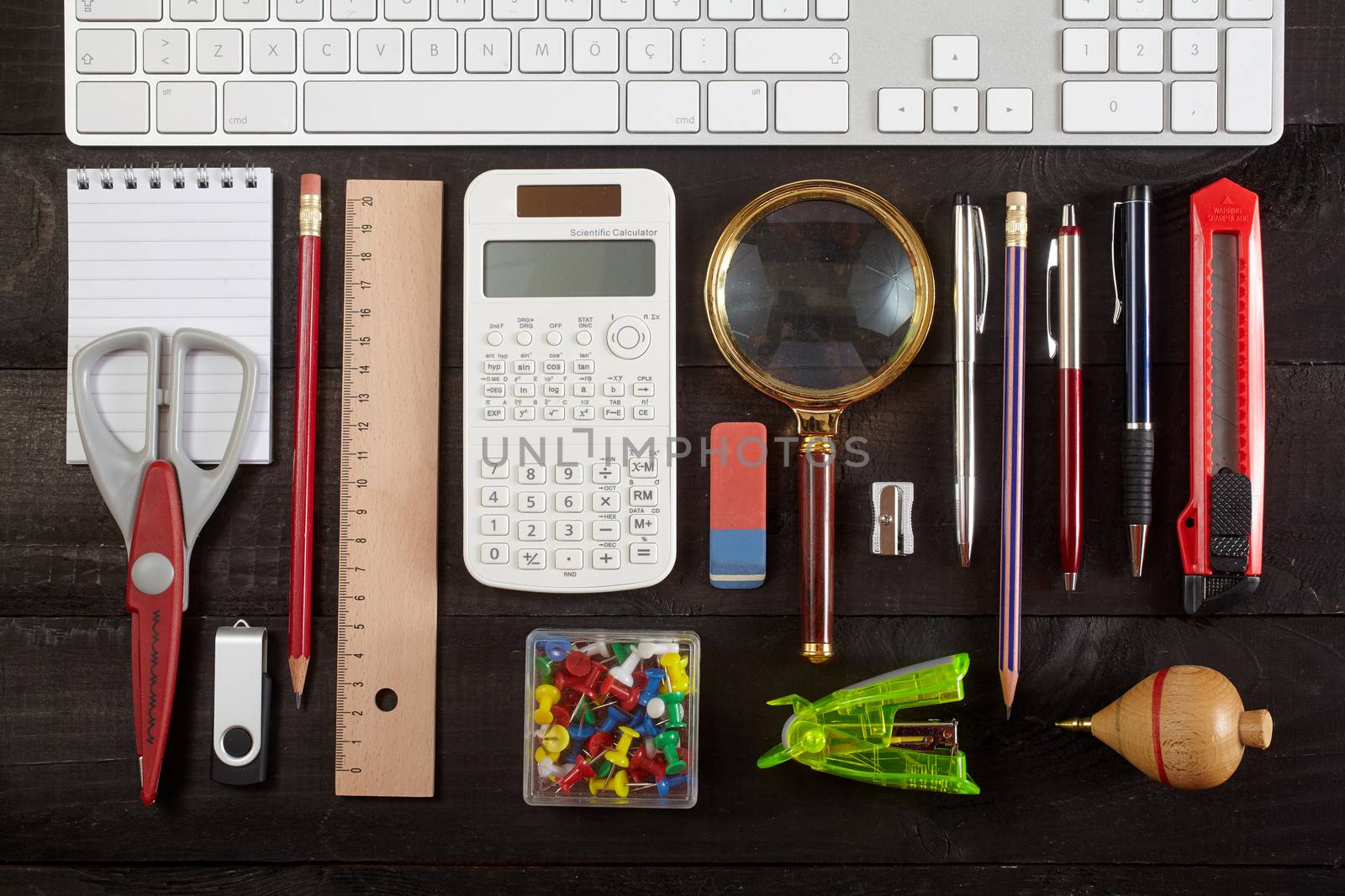 Top view office workplace - keyboard, pencil, calculator, ruler, magnifying glass, pen, cutter, scissors, whirligig and notebook on black table