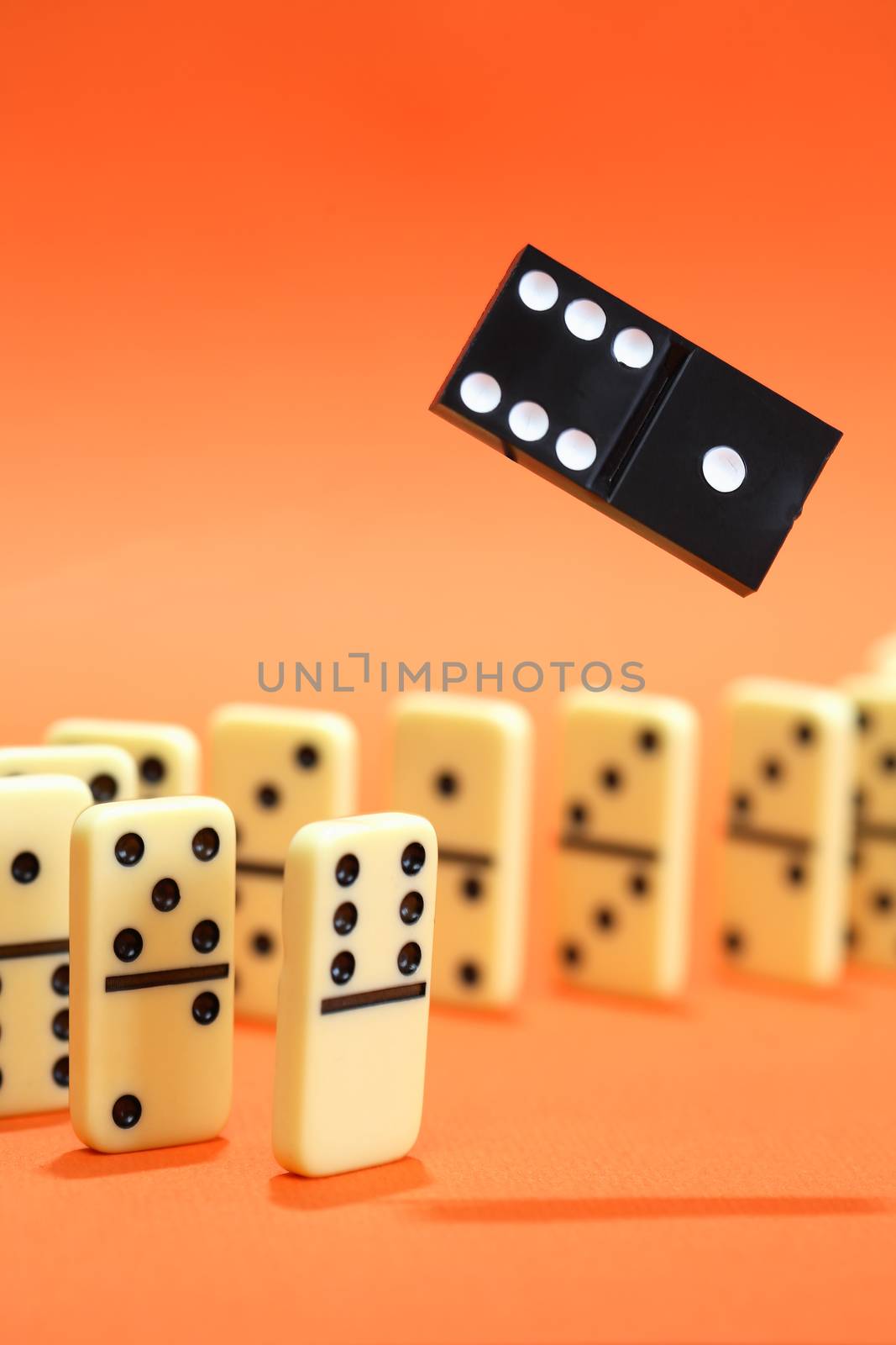 White dominoes standing in a row on red background. One black domino above