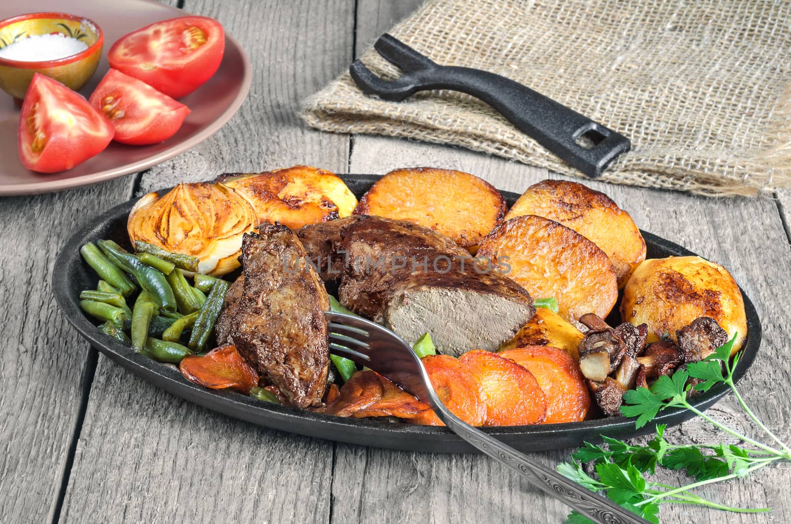 Fried beef liver with vegetables, pan-fried halves of potatoes, onions, whole mushrooms, carrots and green beans on the old boards.