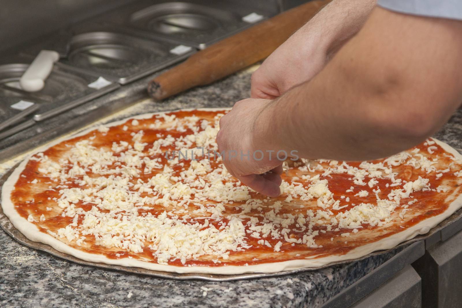 Man chef with raw pizza. Young male in uniform preparing pizza on table.