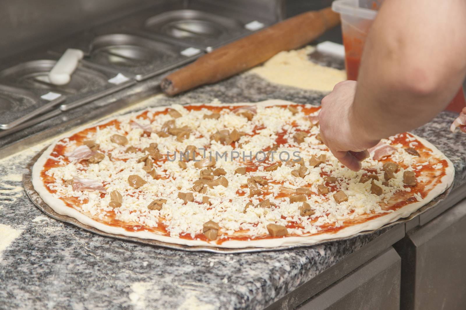 Man chef with raw pizza. Young male in uniform preparing pizza on table.