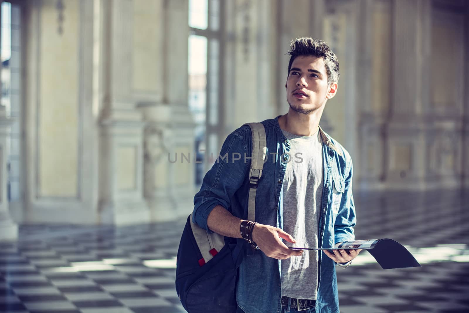 Half Body Shot of a Thoughtful Handsome Young Man, Holding a Guide, Looking Away Inside a Museum