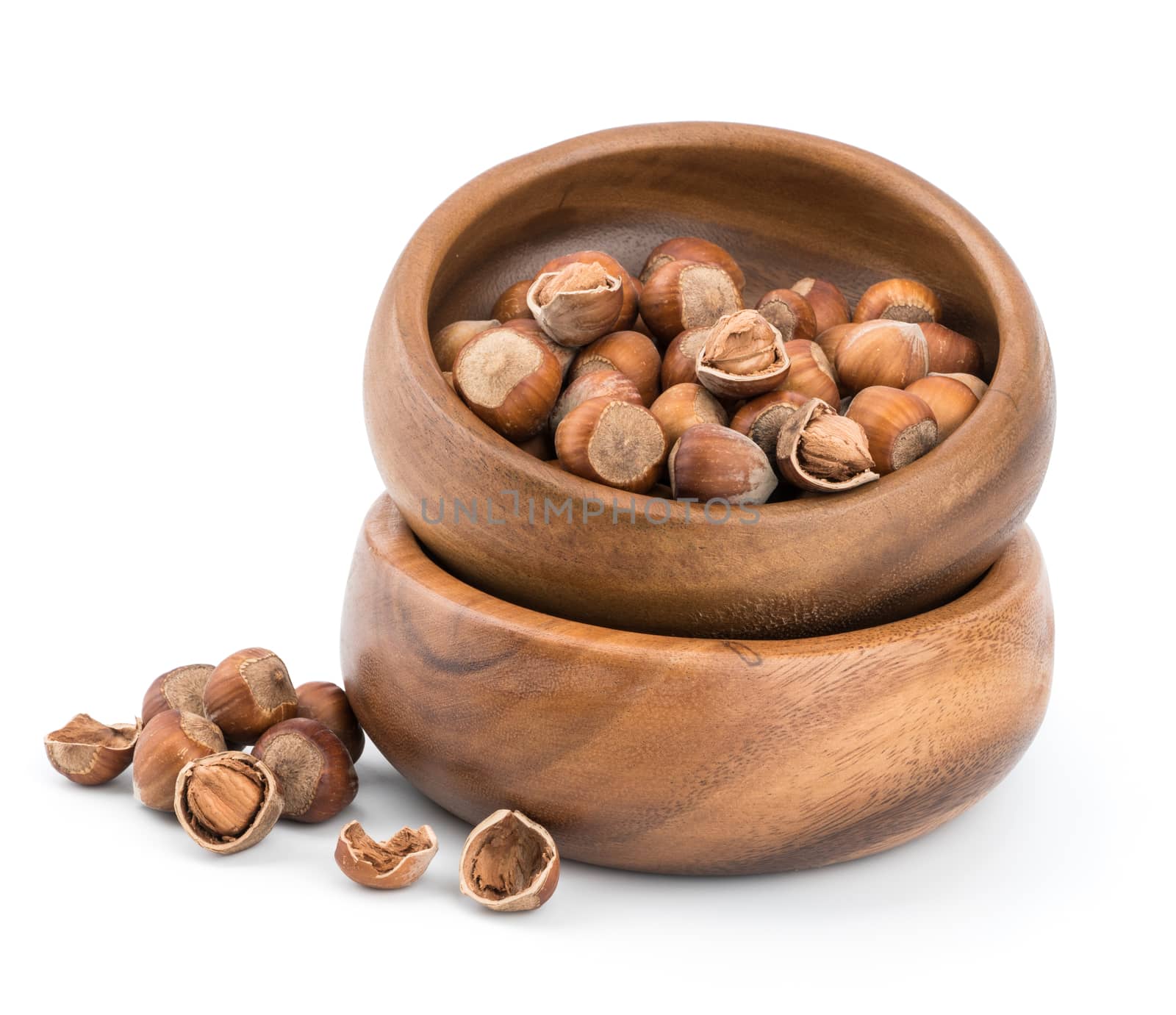 Hazelnuts in a beech wood bowl and loose isolated over white background.