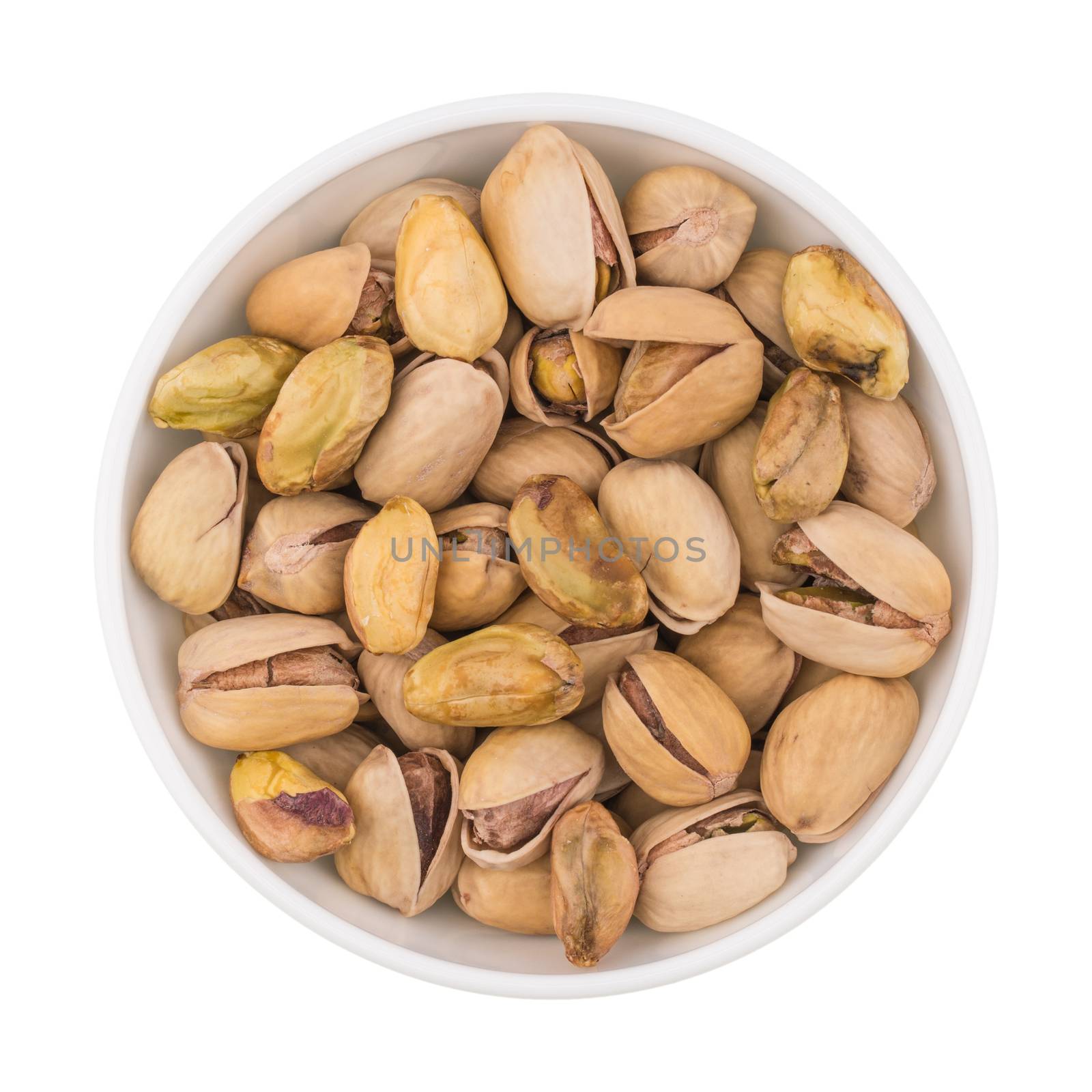 At the center of the frame white bowl with pistachio nuts on a white background. Salted roasted pistachios. Close. Horizontal shot. Top view.