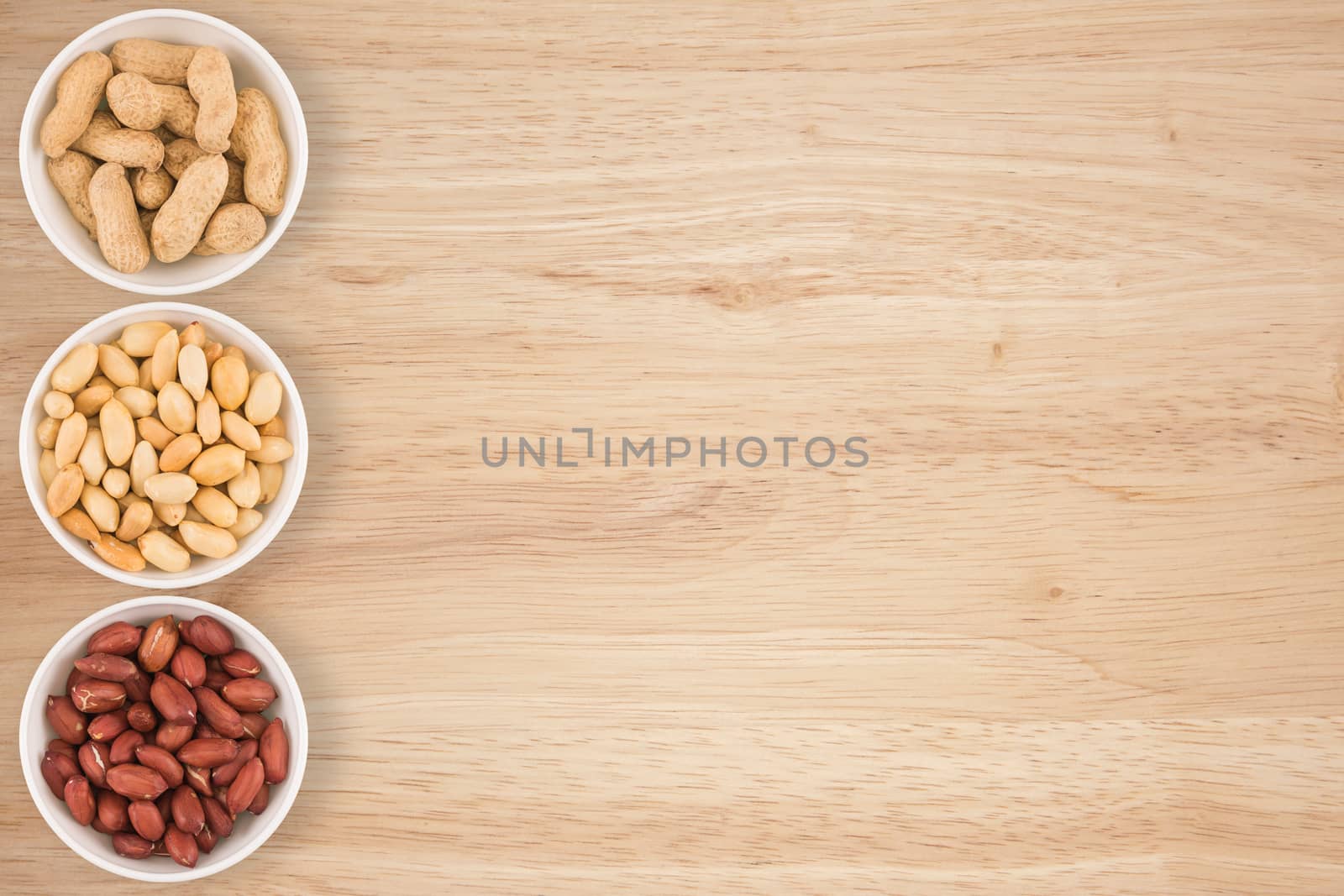 Some peanuts in a cyan bowl on a wooden table.