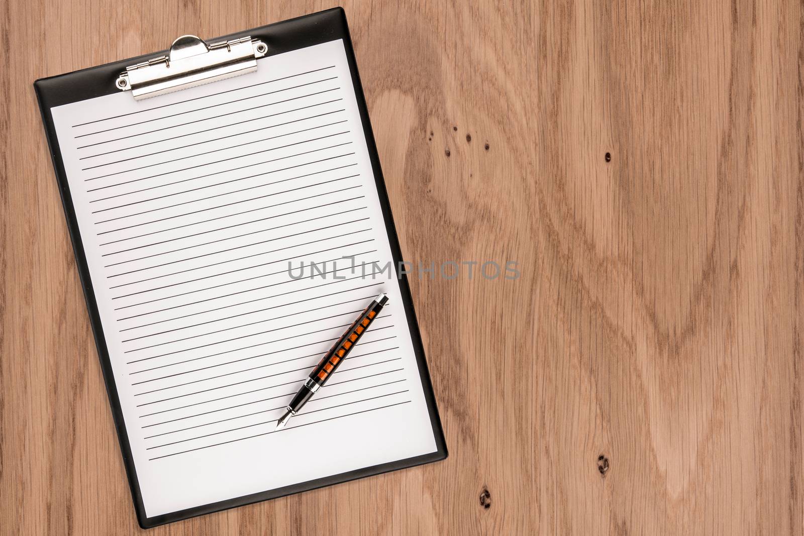 Clipboard with blank paper and pen on wooden desk. Copy space for text