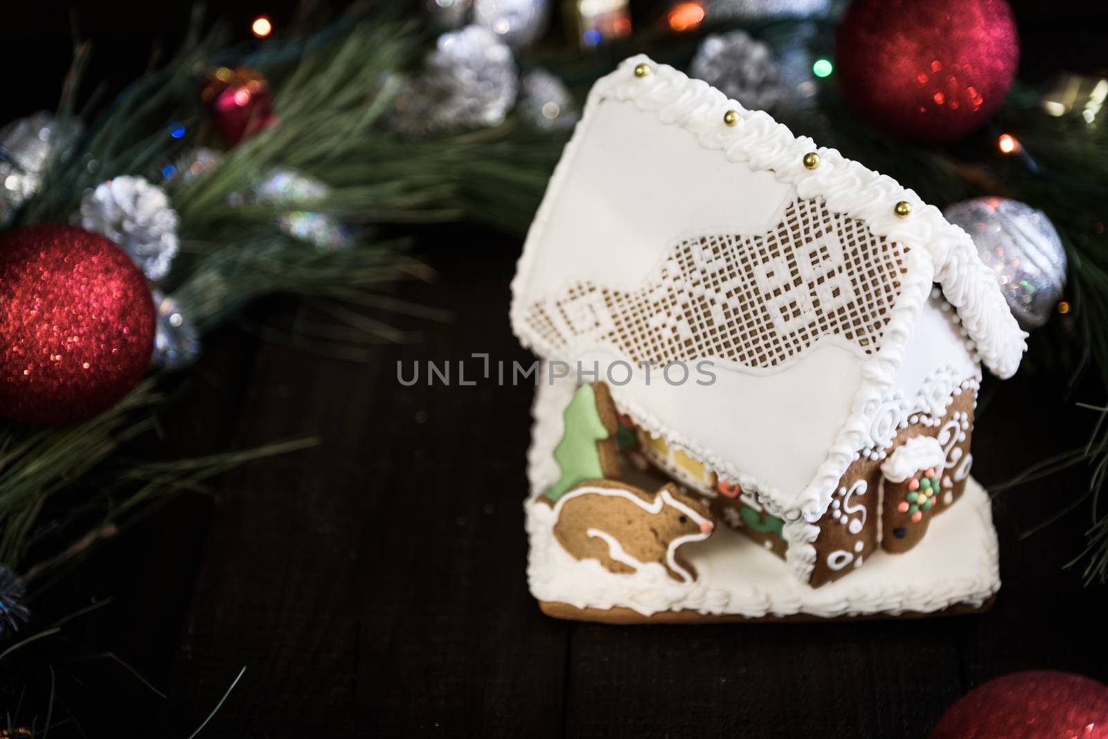 the gingerbread house in the white glaze on the background of the Christmas wreath with Christmas decorations