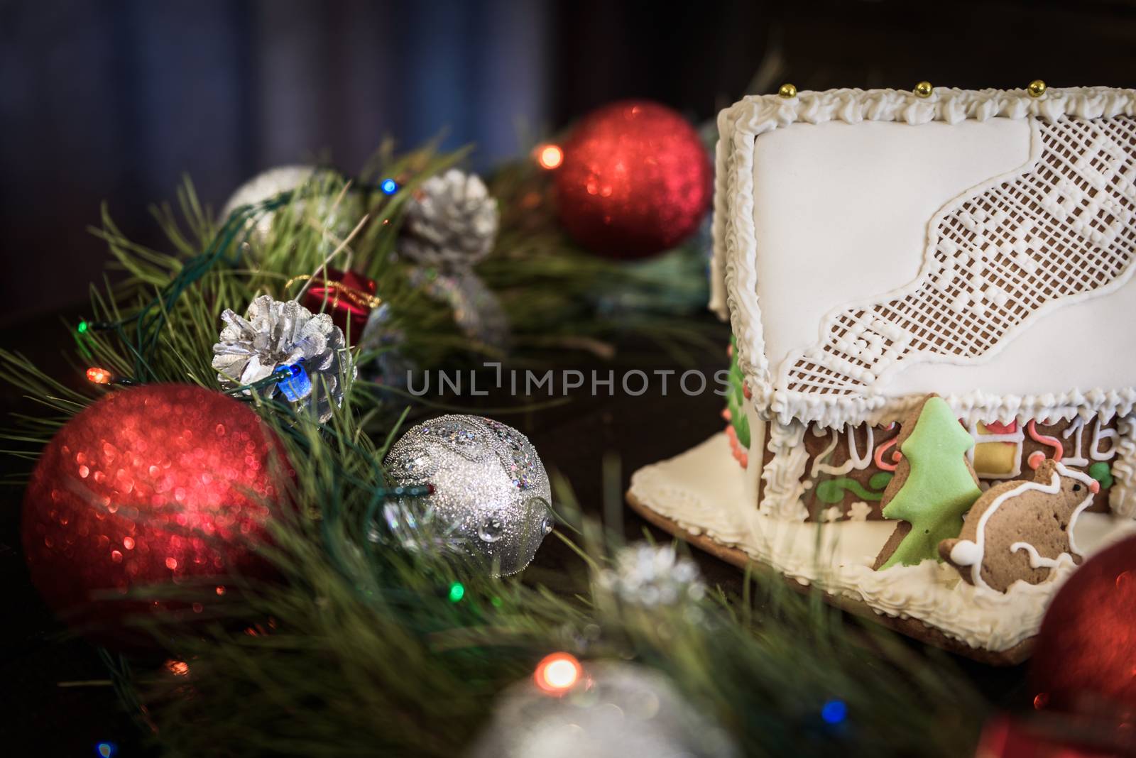 the gingerbread house in the white glaze on the background of the Christmas wreath with Christmas decorations