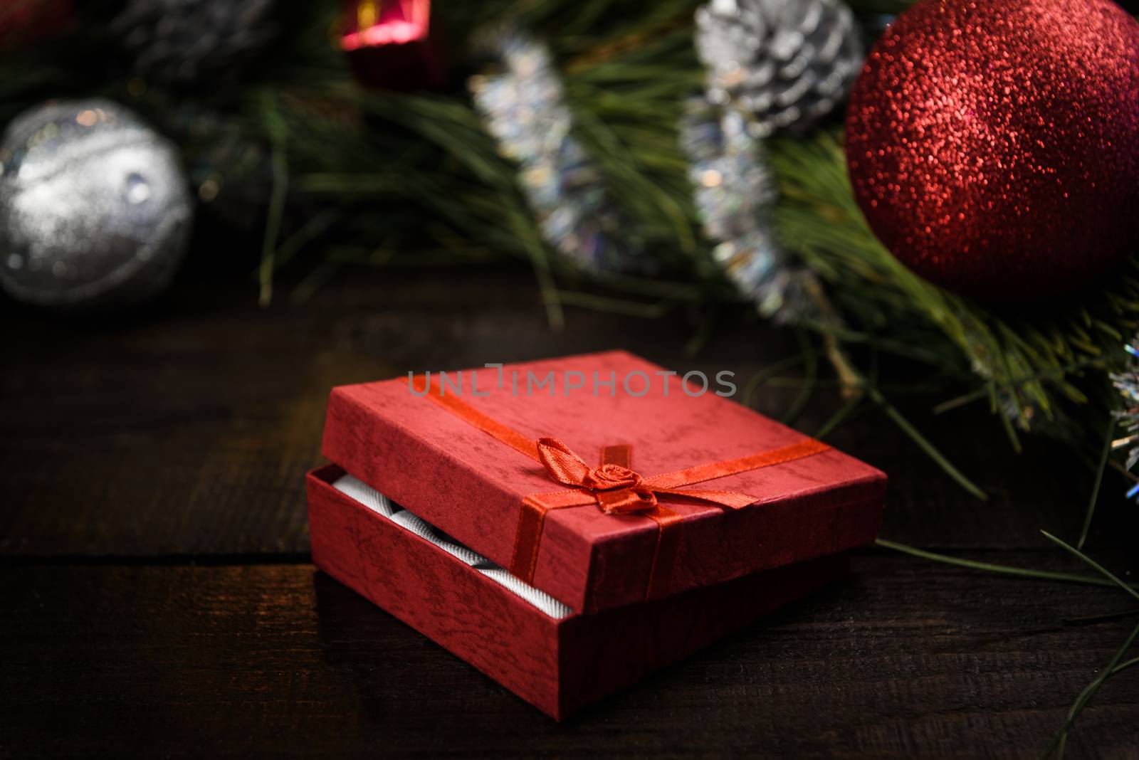 Christmas gift in red box with red ribbon on wooden background, surrounded by a Christmas wreath