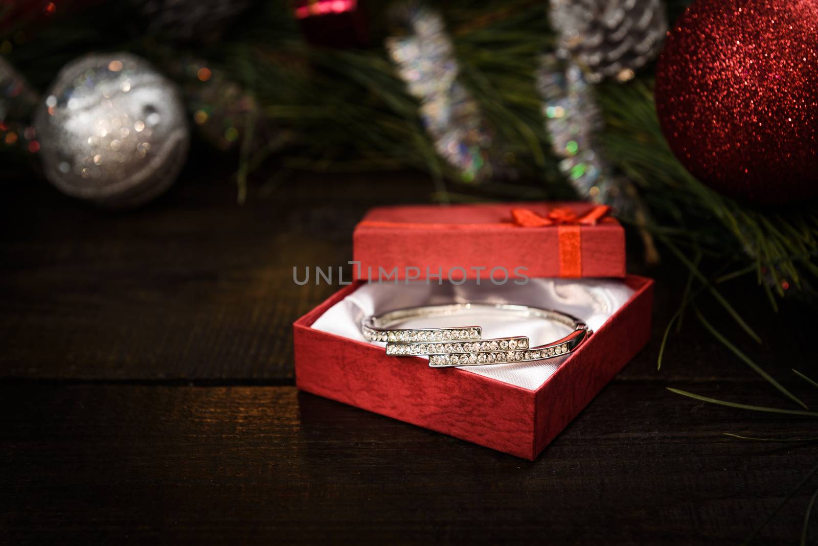 Christmas gift in red box with red ribbon on wooden background, surrounded by a Christmas wreath