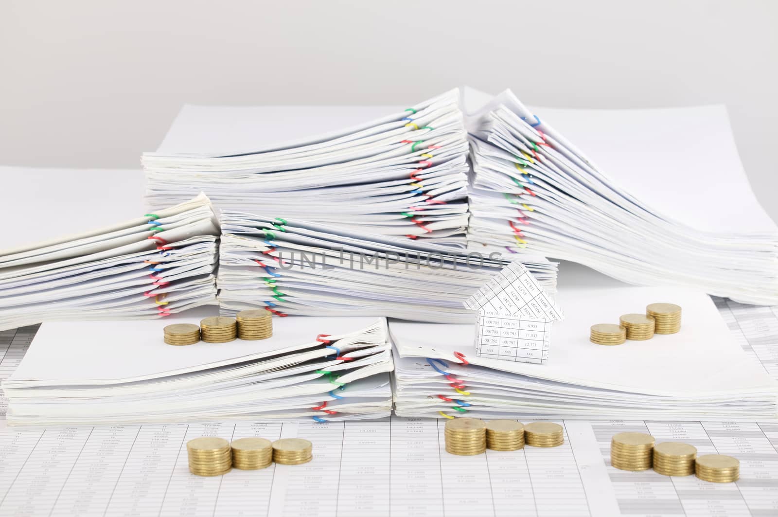 House with step pile of gold coins on pile overload paperwork of report and receipt with colorful paperclip place on finance account with white background.