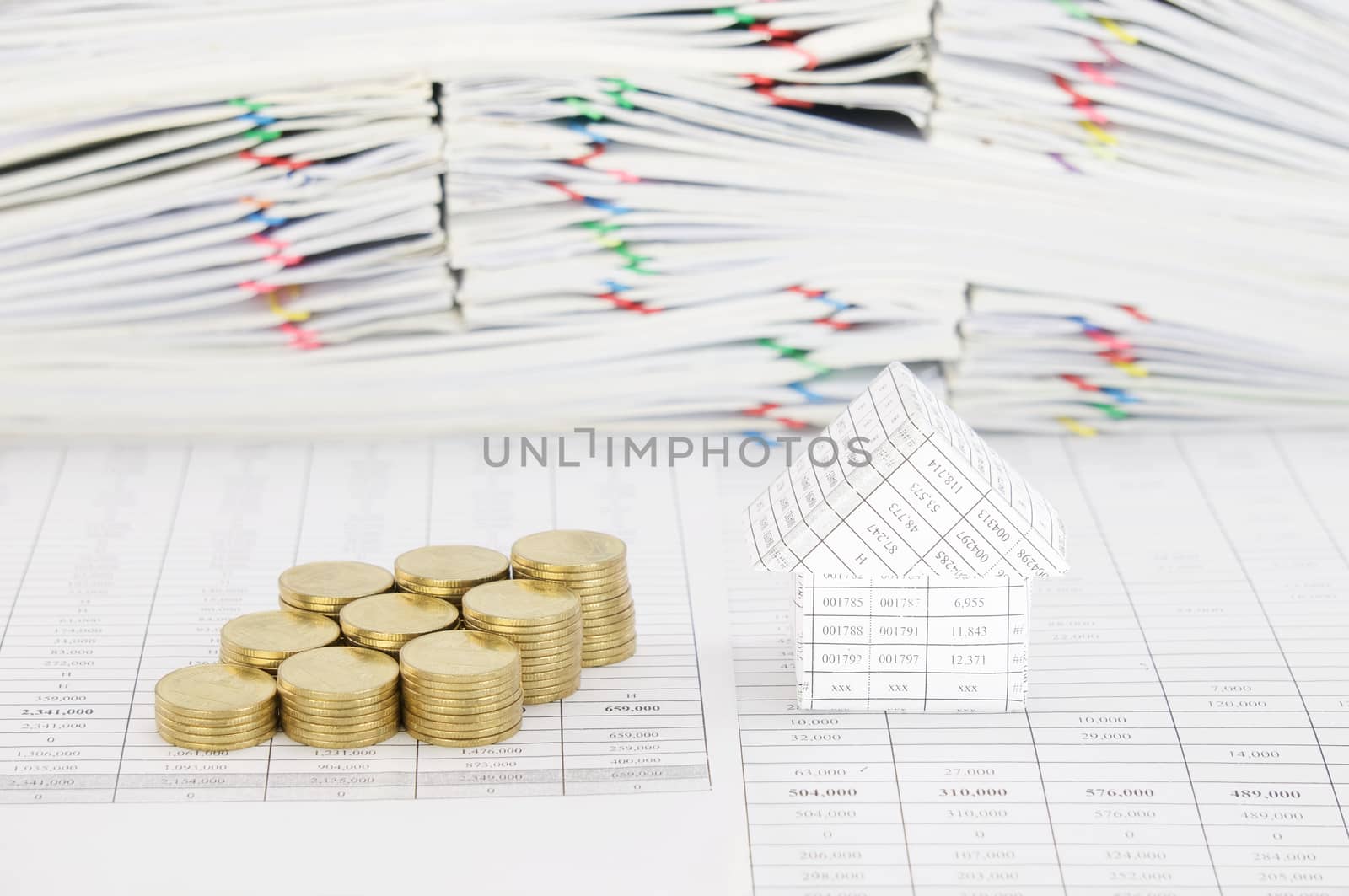 House and step group of gold coins on finance account have blur pile overload paperwork of report and receipt with colorful paperclip as background.