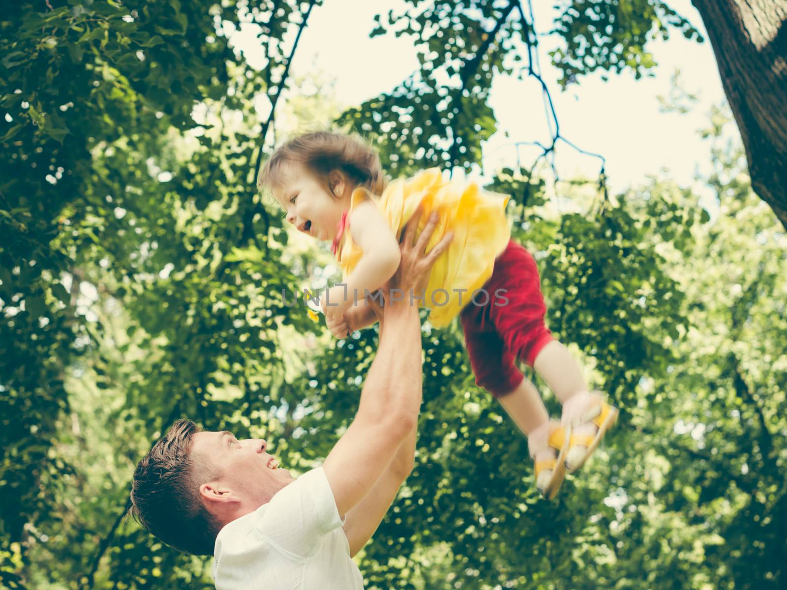 Dad and his little one-year old daughter having fun. Father throws up his little girl. Colorful image for modern life family concept