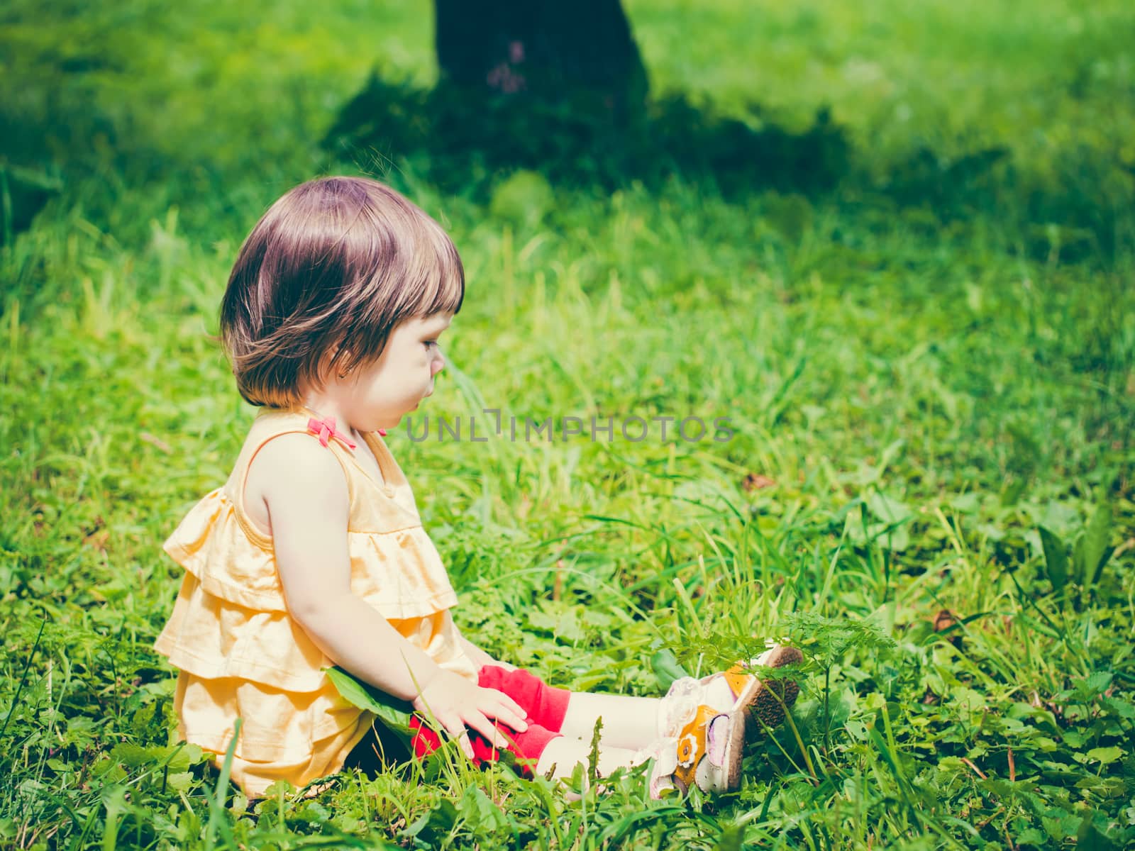 One year old baby girl sitting on grass and looking away. Colorful image with copy space