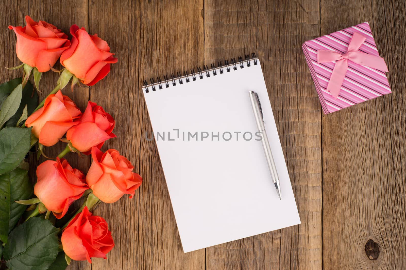Blank notebook, pen with a rose and a gift on a wooden table