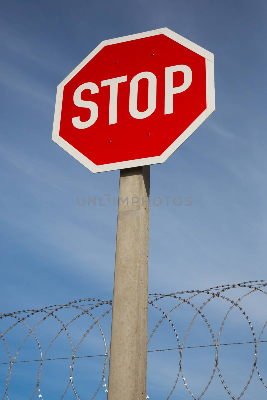 Bright red stop sign against blue sky and razor wire coil