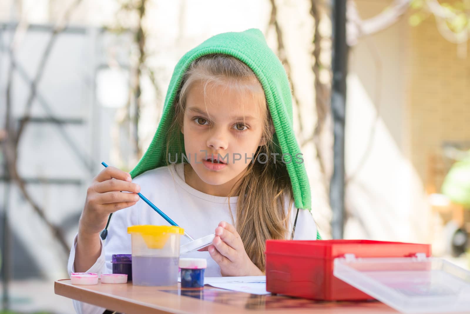 Girl draws paints in the yard in the spring sunny day and looked into the frame