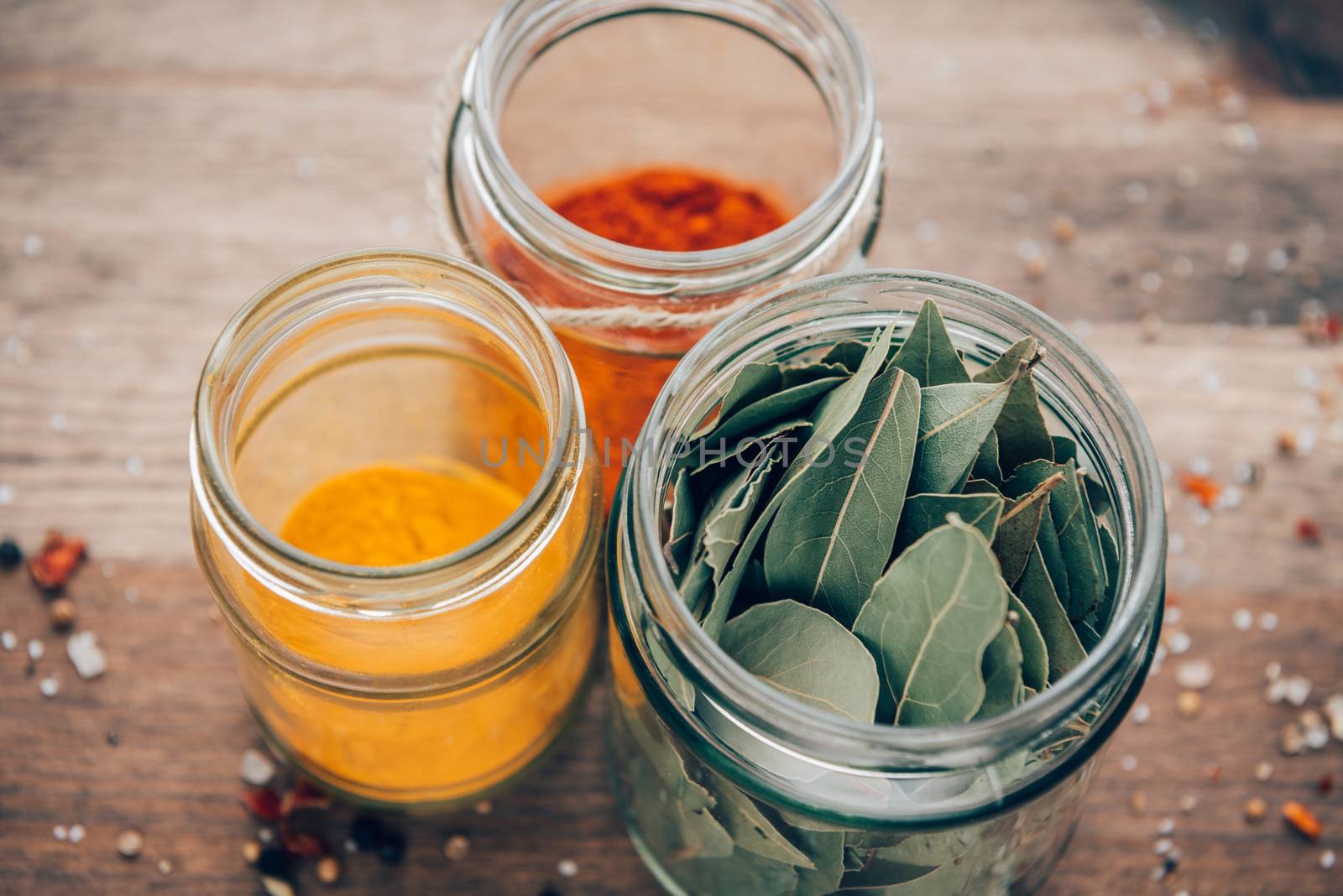 Bay leaves, turmeric and paprika powder in jars on a wooden table.