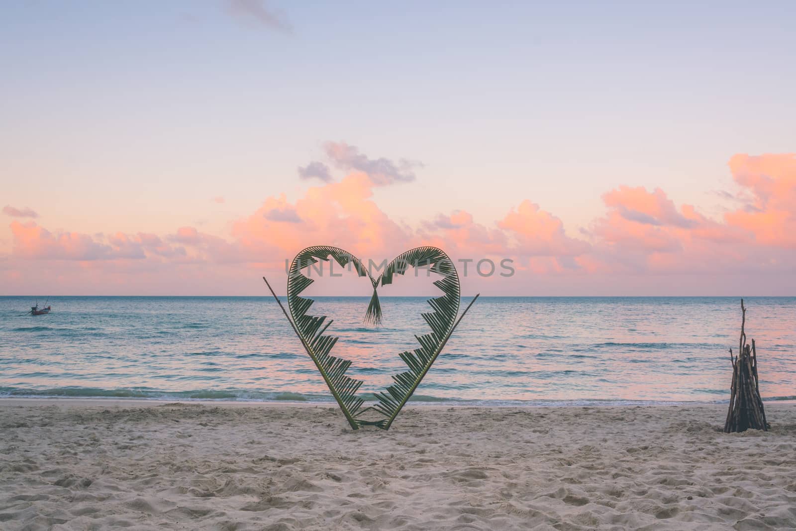 Palm branches tied into the shape of a heart on the beach.  by kargoo