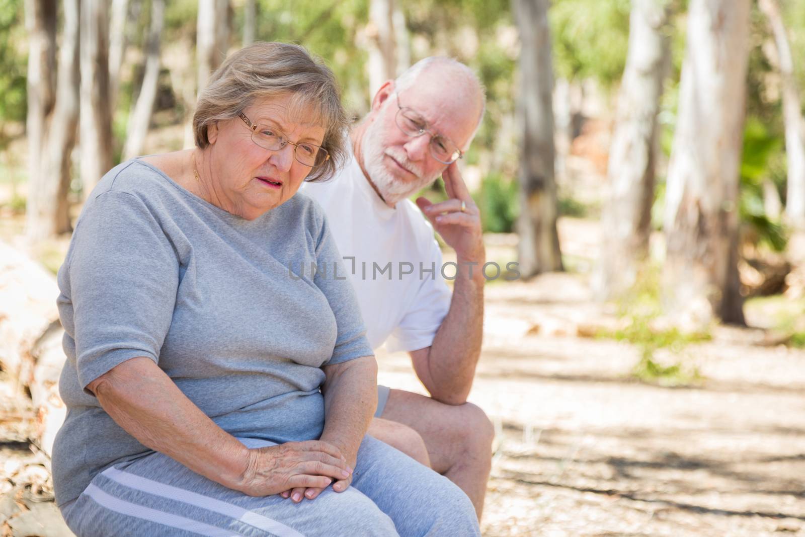 Upset Senior Woman Sits With Concerned Husband Outdoors by Feverpitched