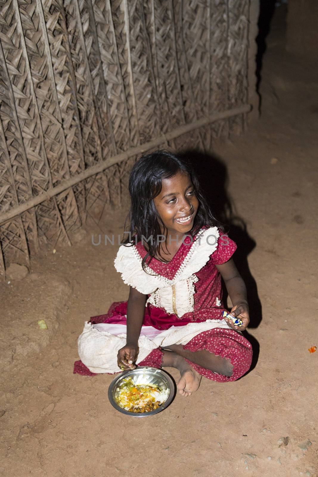 Documentary editorial image. Pondicherry, Tamil Nadu, India - April 24 2014. Very poor young girl sitting in the street, eating on the floor during the night. Poverty