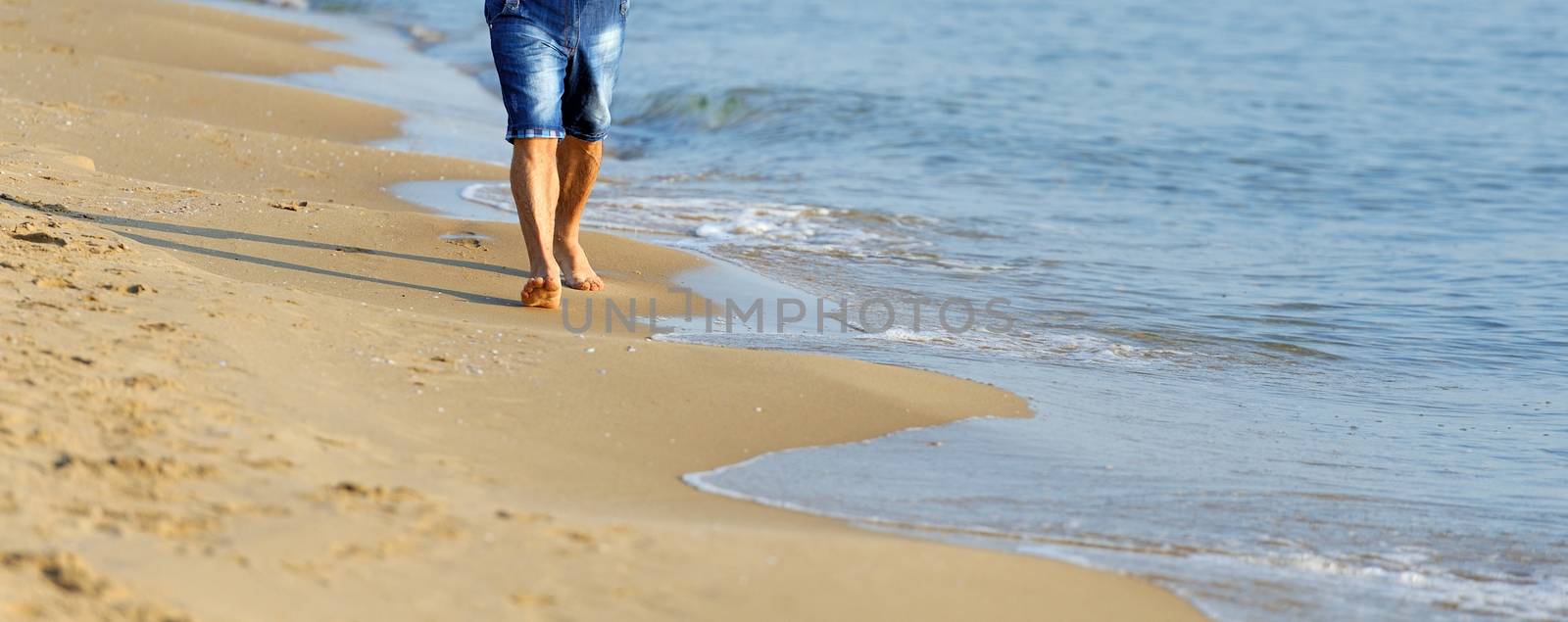 Man walking on sand beach. Closeup detail of man feet and golden sand on beach