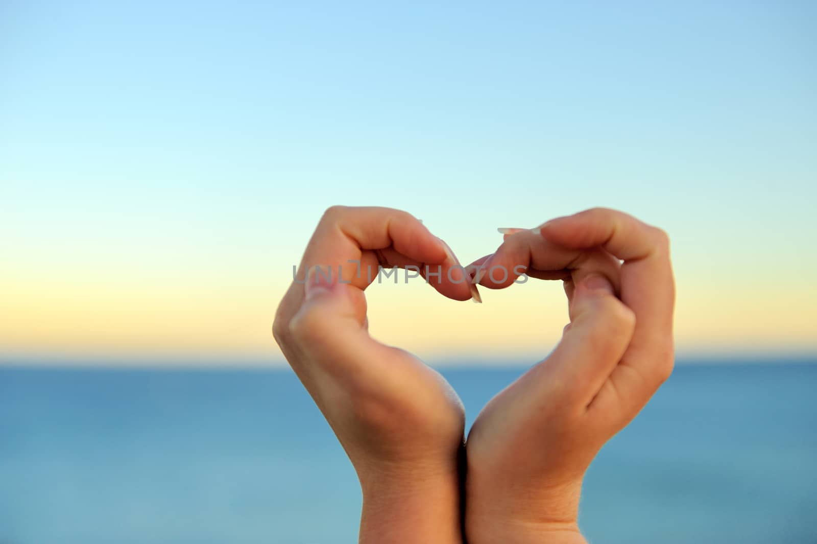 Female hand making a heart shape against a beautiful blue sky