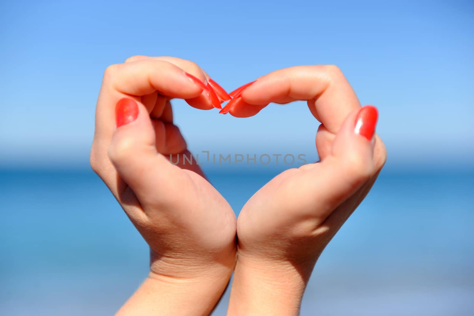 Female hand making a heart shape against a beautiful blue sky