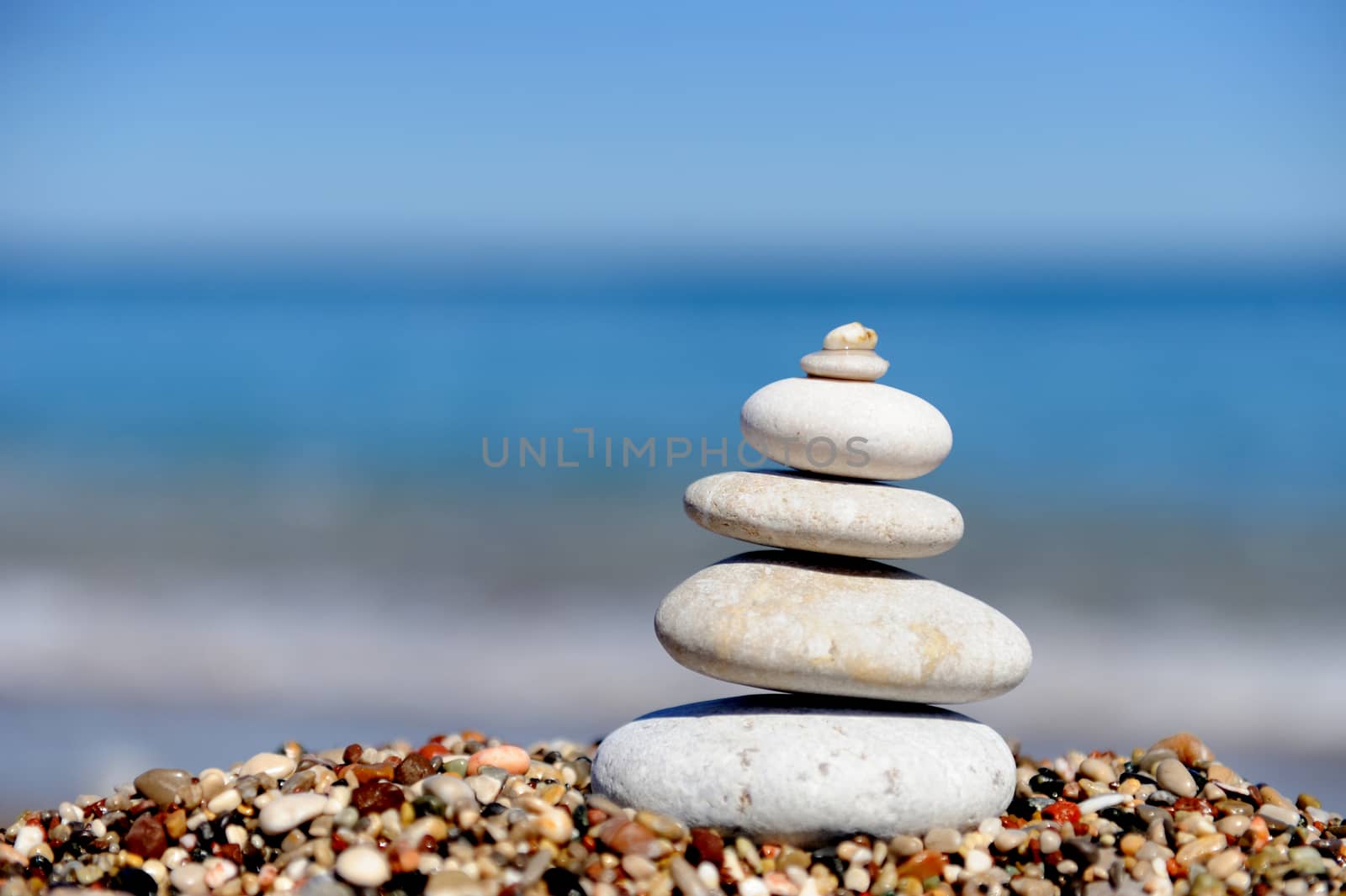 Stack of pebbles on a big rock at the beach on the blue background