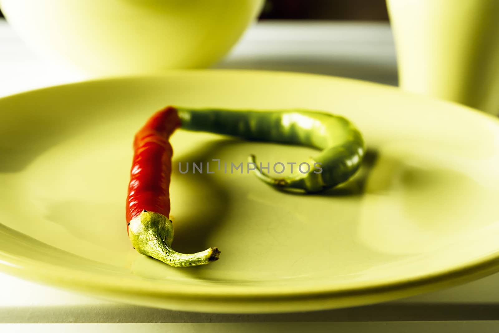 Red and green hot pepper on green dish over white wood. Horizontal image.