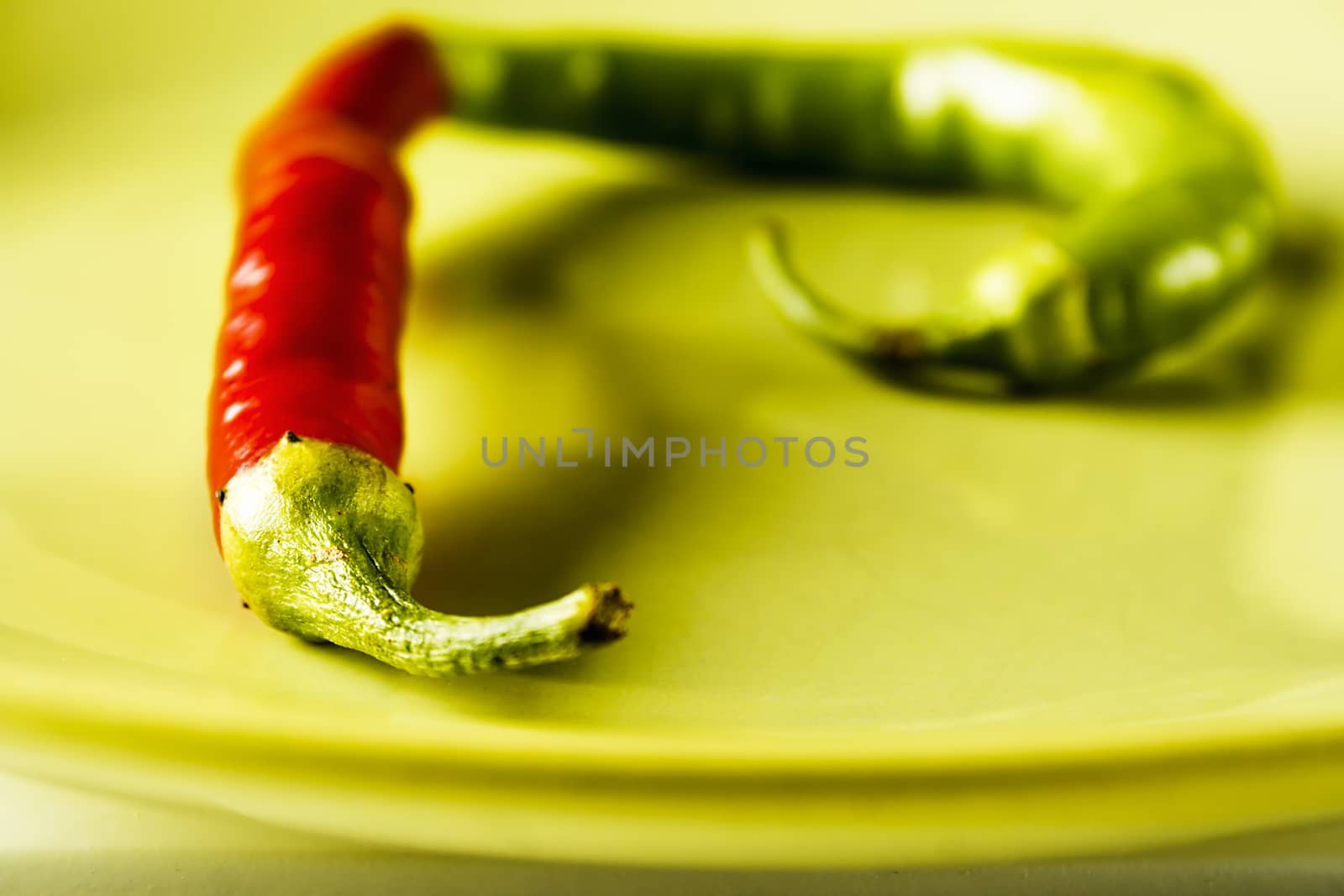 Closeup red and green hot pepper on green dish over white wood. Horizontal image.