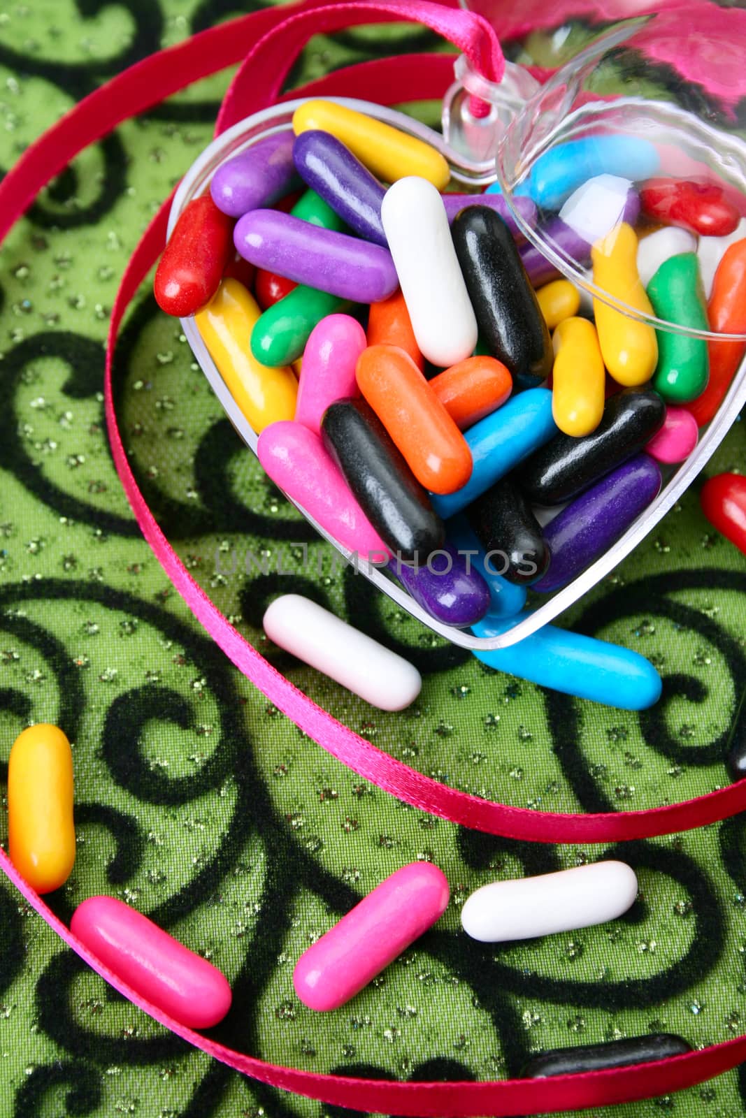 Colorful candies in a heart container on green background