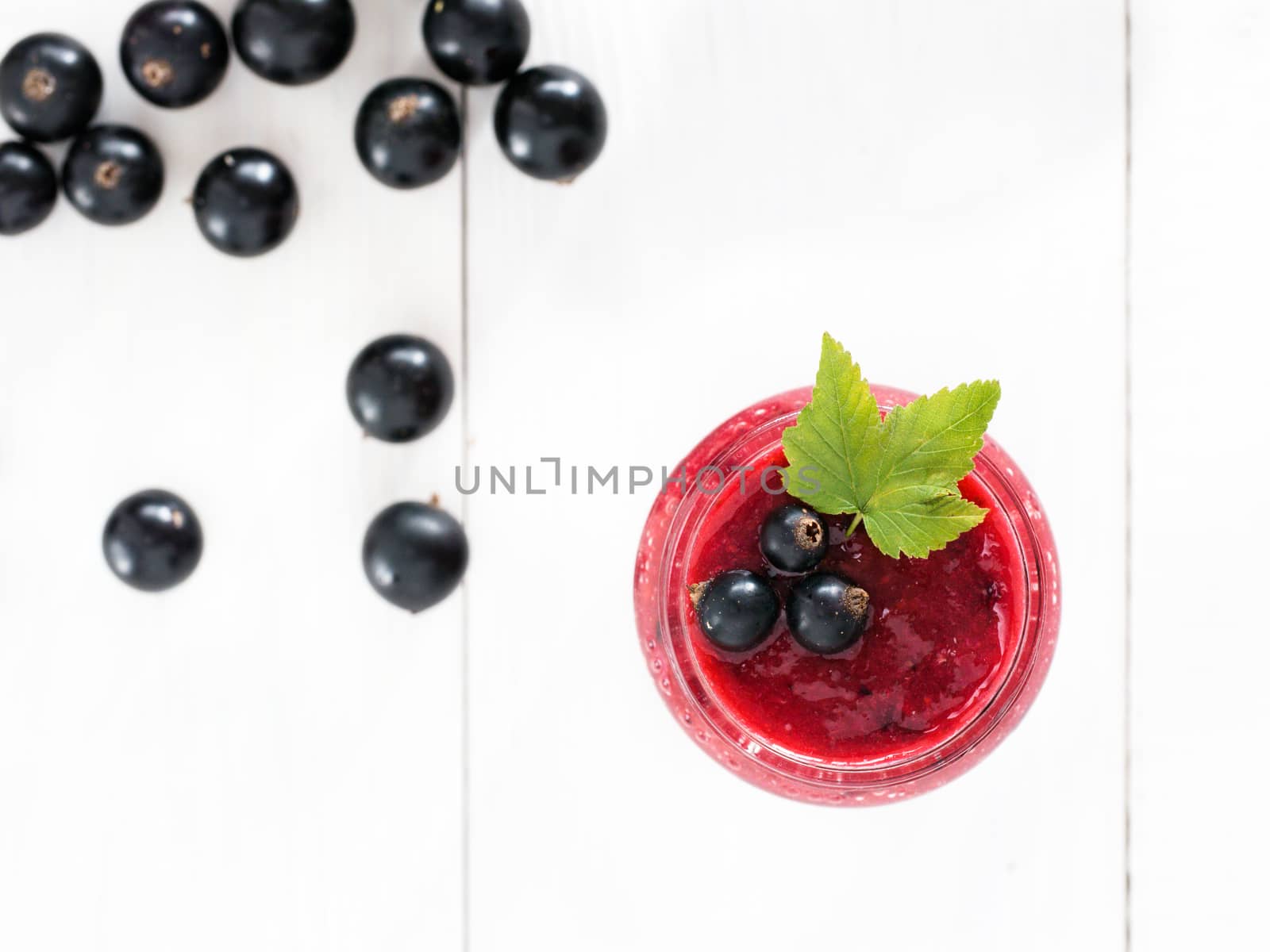 Delicious black currant smoothie in glass jar with fresh berries on white wood background. Top view or flat lay