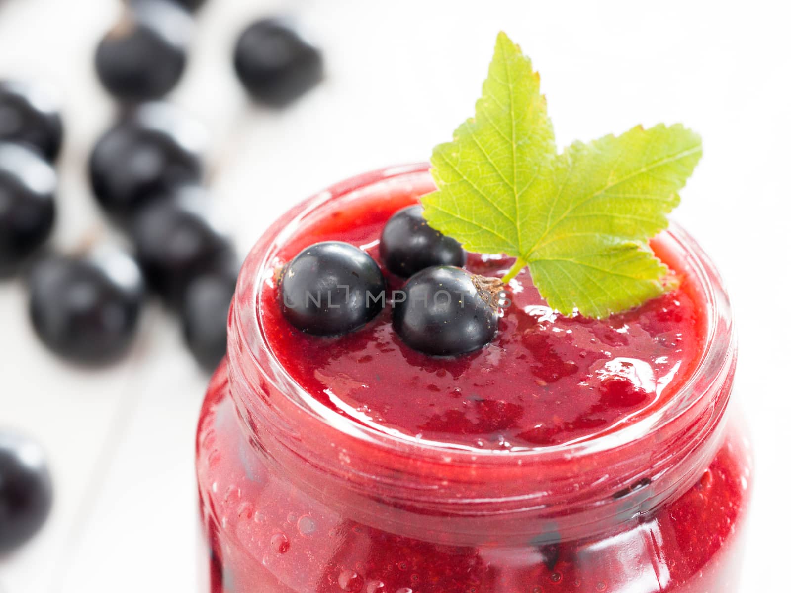 Delicious black currant smoothie or jam in glass jar with fresh berries on white wood background. Shallow DOF. Selective focus