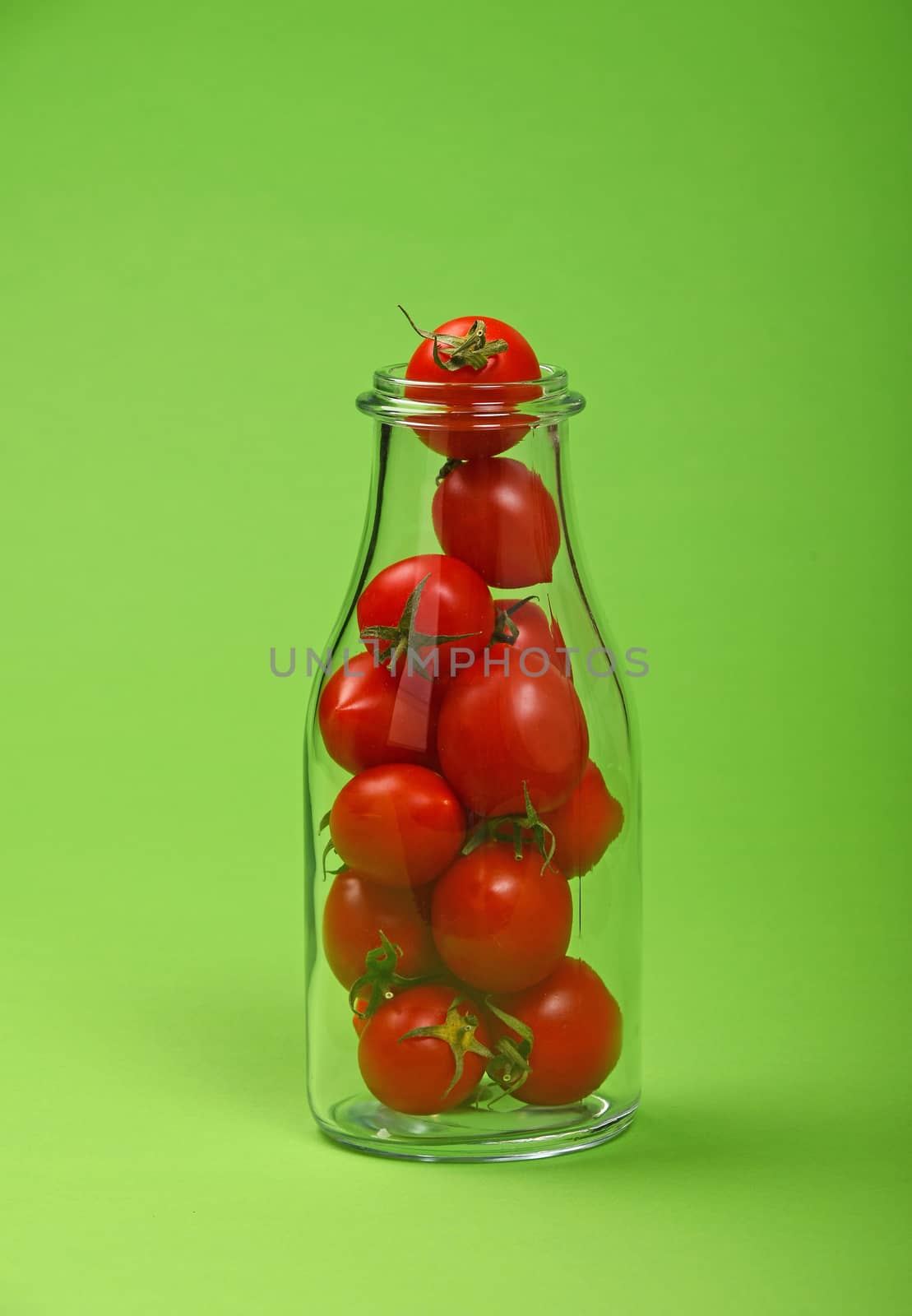 Big glass bottle full of red cherry tomatoes over green background as symbol of fresh natural organic juice or ketchup
