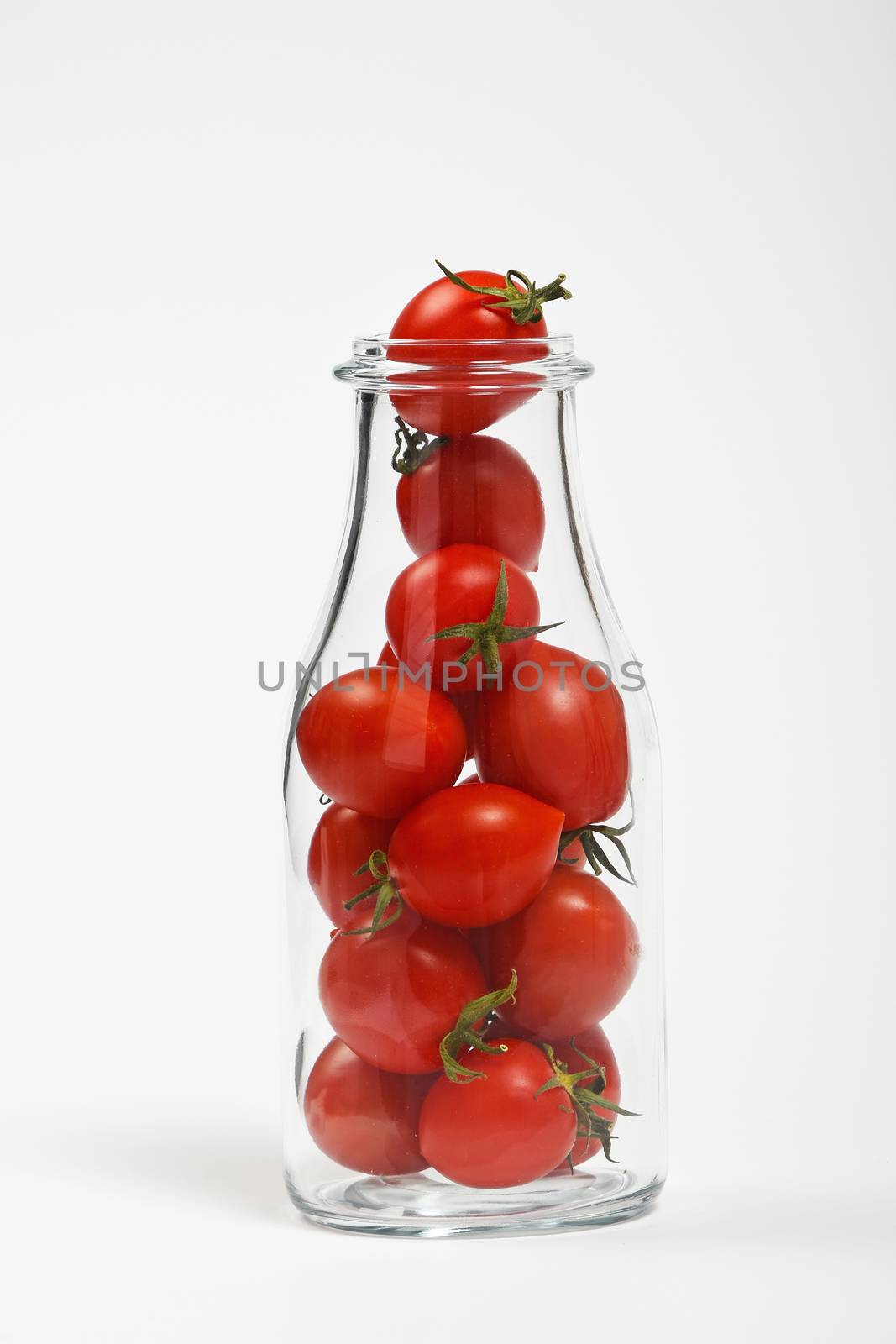 Big glass bottle full of cherry tomatoes over white background as symbol of fresh natural organic juice or ketchup