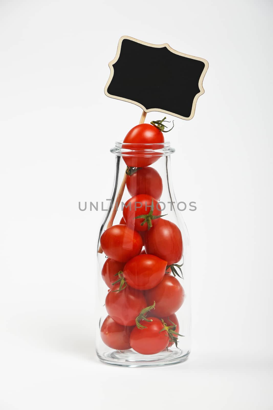 Big glass bottle full of cherry tomatoes and black chalkboard sign over white background as symbol of fresh natural organic juice or ketchup
