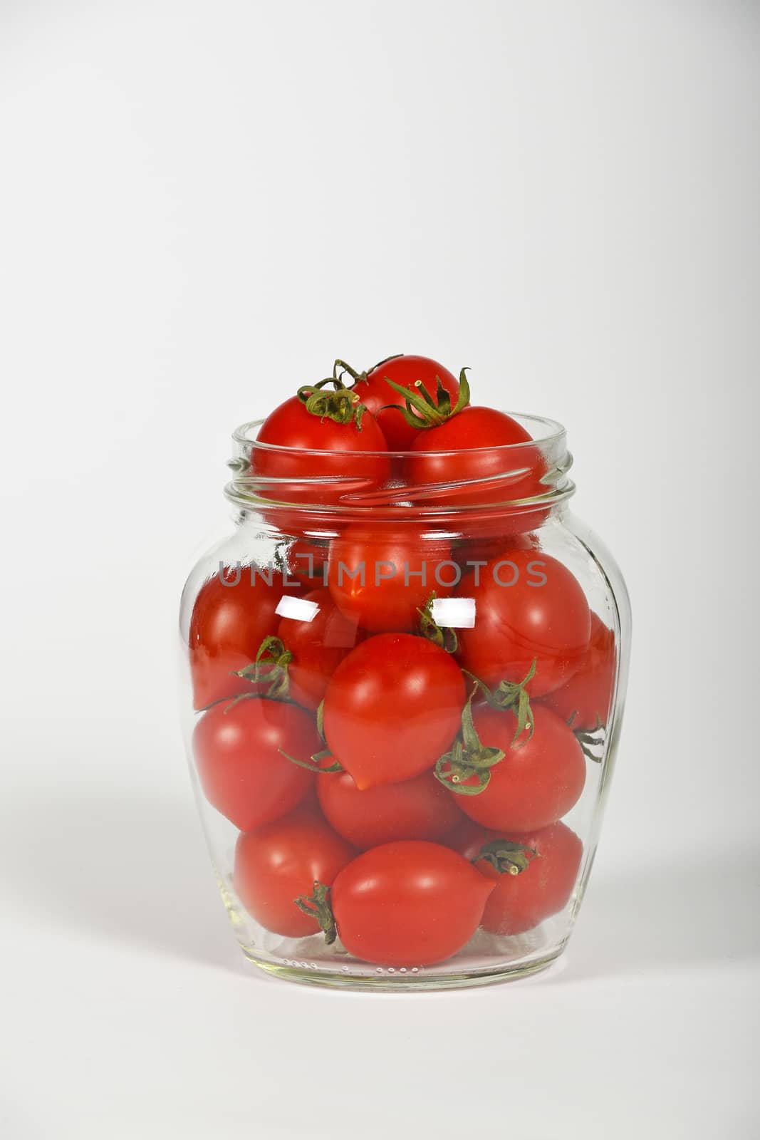 Glass jar full of red cherry tomatoes ready to pickle for conservation over white background, side view