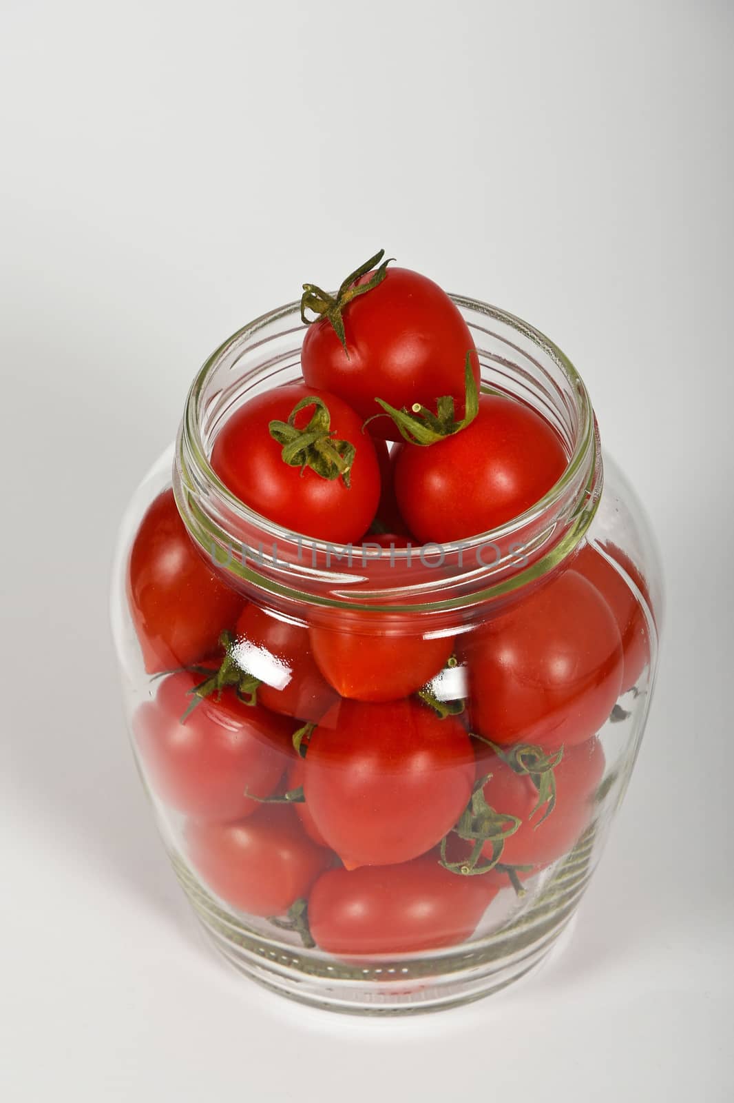 Glass jar full of red cherry tomatoes ready to pickle for conservation over white background, high angle view, close up