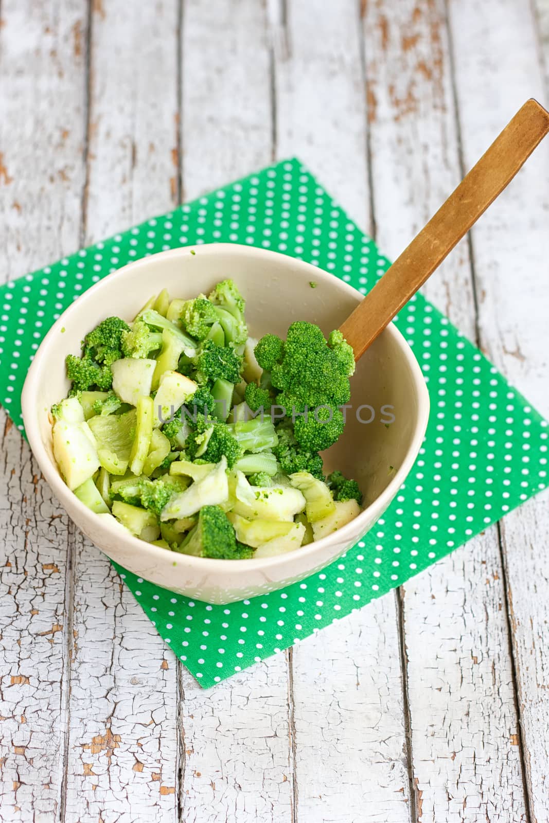 Salad in a deep bowl, broccoli, pepper and apple. On a wooden background