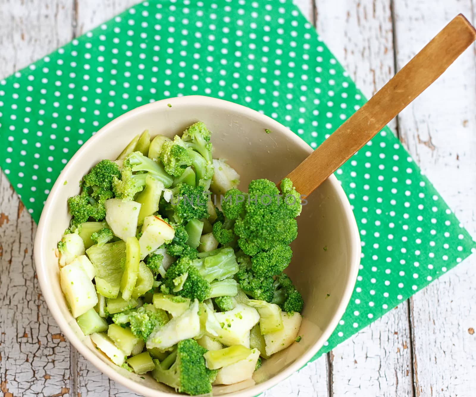 Salad in a deep bowl, broccoli, pepper and apple. On a wooden background